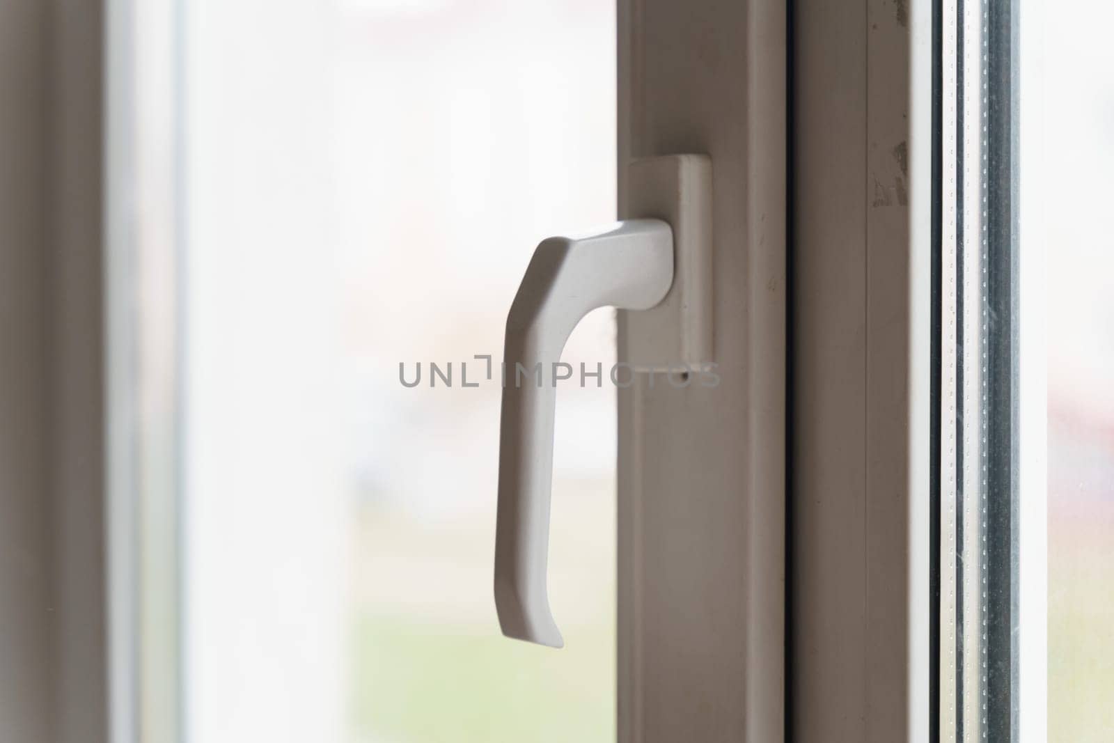 A sharp focus on a white window handle with soft natural light filtering through the glass, indicating a daytime setting.