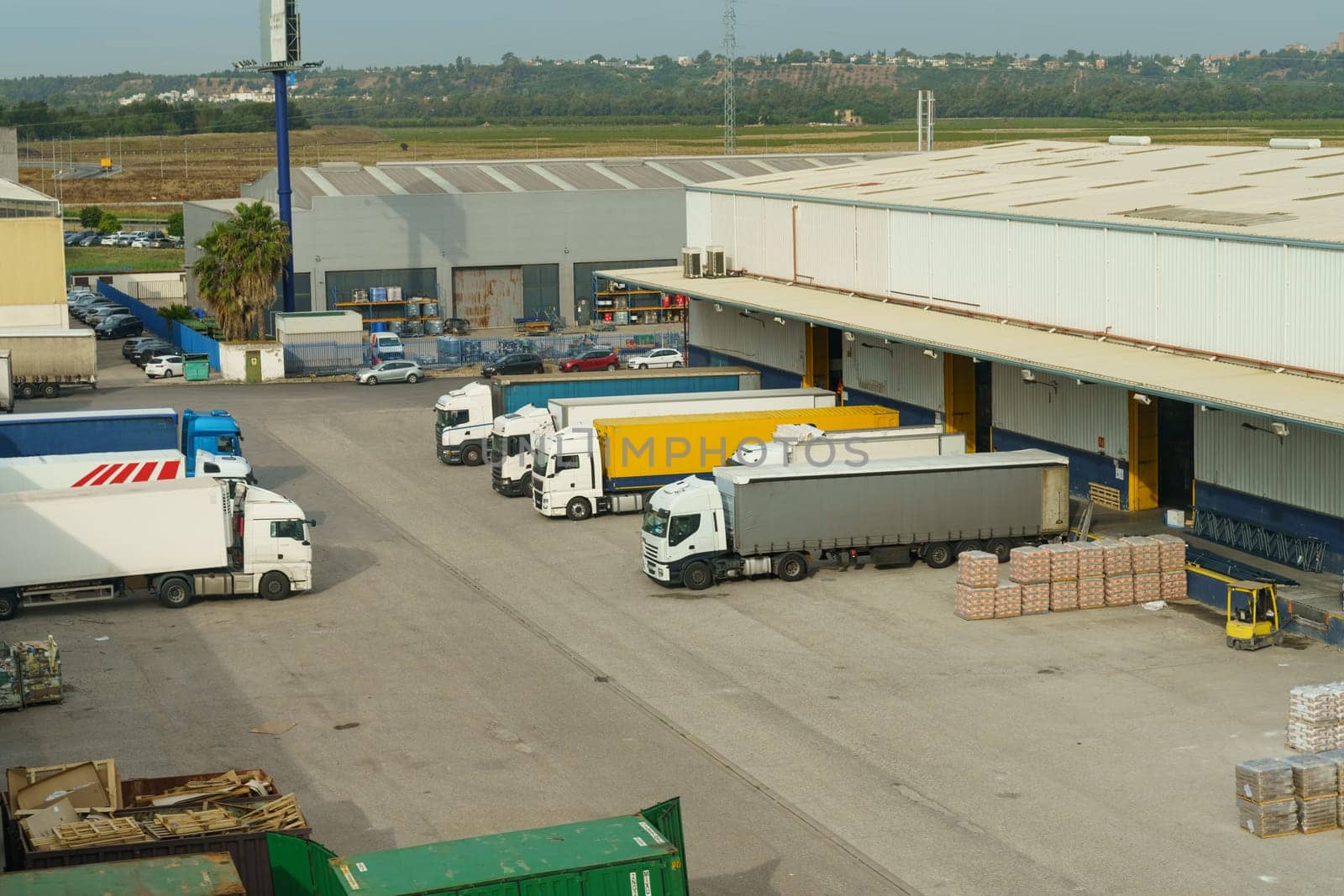 Multiple trucks of varying sizes and colors are parked neatly in rows in a large parking lot dedicated to transport and logistics operations.
