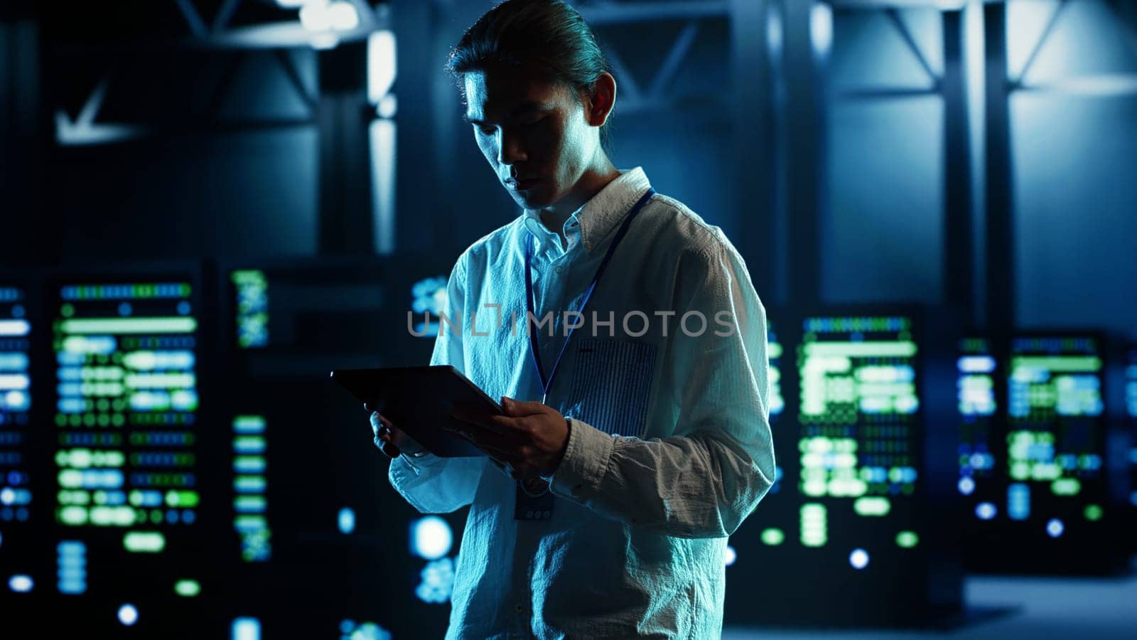 Asian man strolling through data center server rows providing processing and memory resources for different workloads. Engineer monitoring supercomputers tasked with solving complex operations