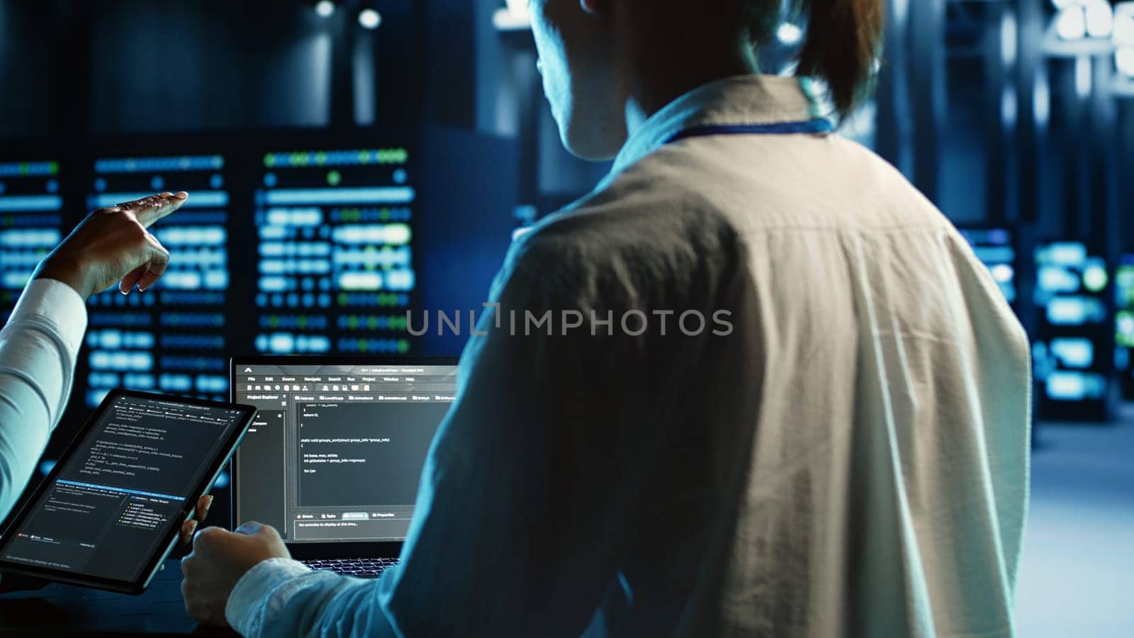 Engineering team members running code on tablet and laptop, updating professional data center equipment designed to accommodate server rigs, networking systems and storage arrays