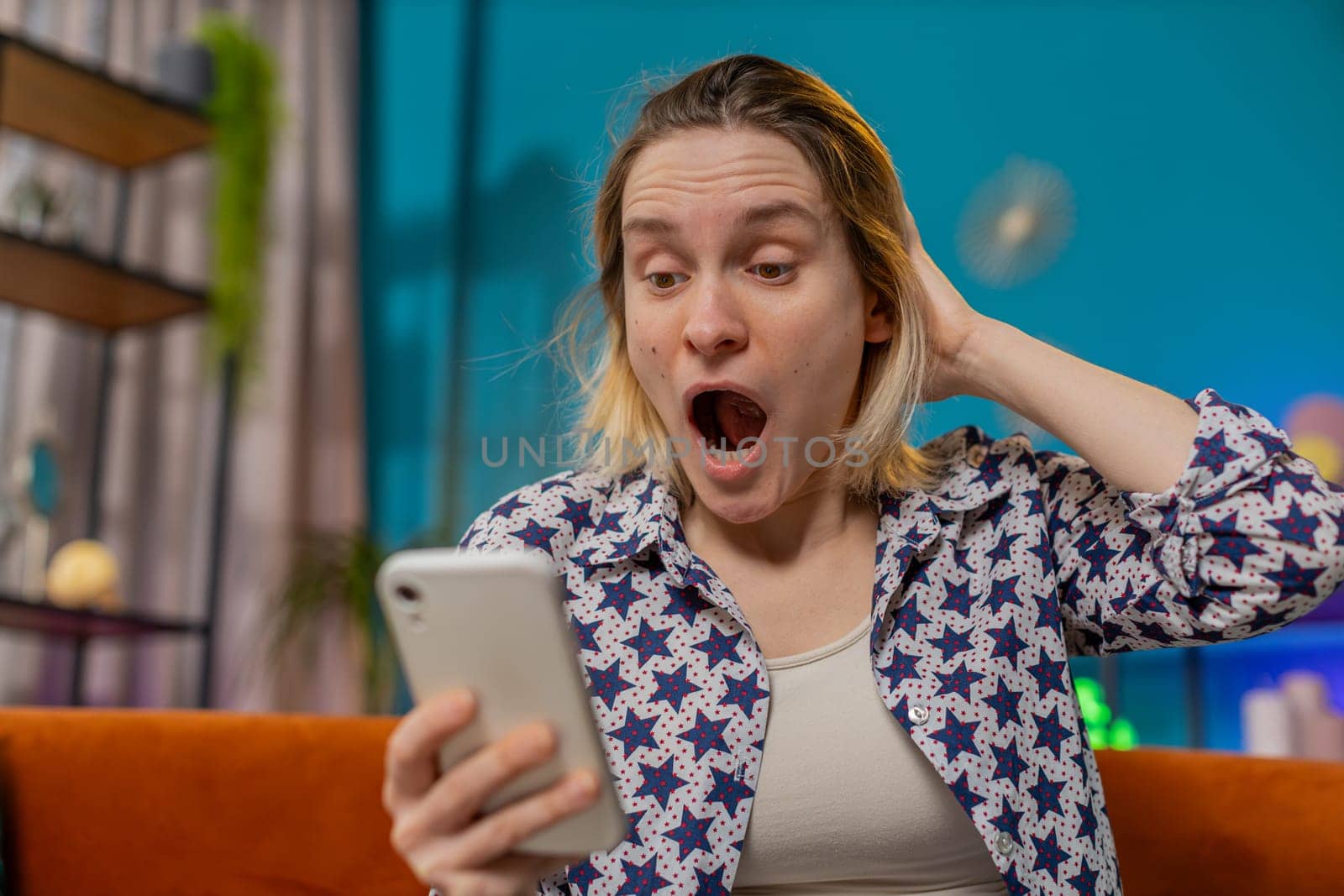Surprised excited amazed woman winner holding smartphone reading good news amazed by online bet bid game win. Happy Caucasian girl sits on sofa looking at screen overjoyed by victory success at home