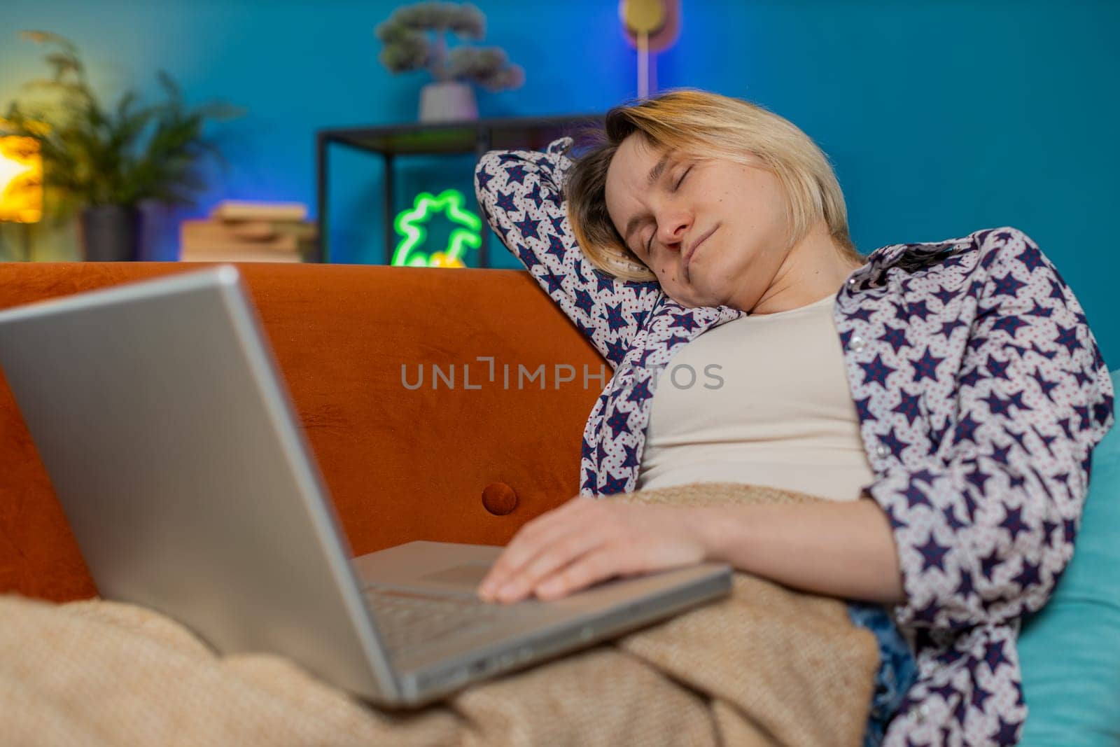 Bored sleepy young Caucasian woman working on laptop computer, leaning on hand sitting on couch with blanket. Exhausted tired freelancer workaholic girl sleeping in living room at home apartments