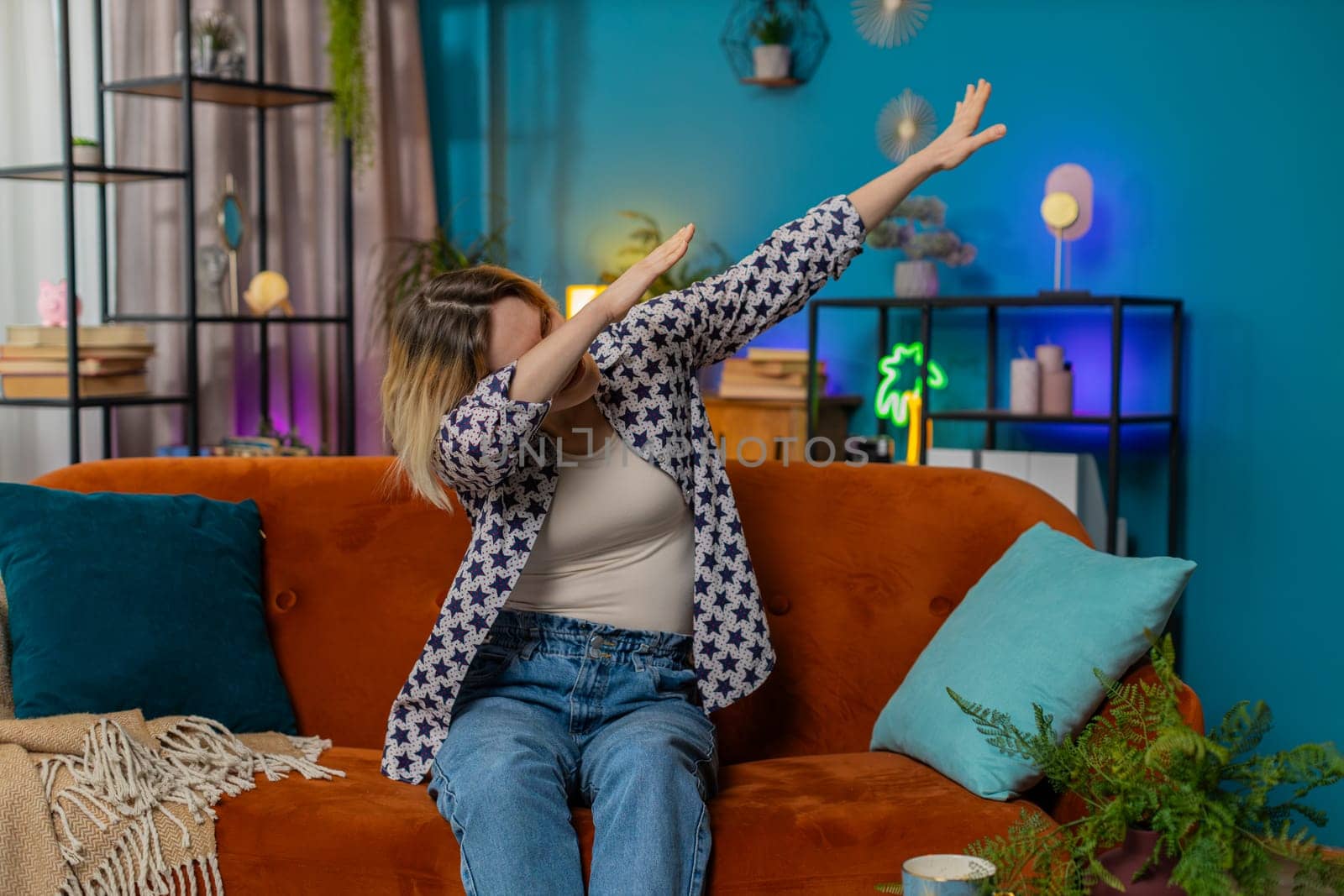 Trendy cheerful positive young woman having fun dancing, dabbing raising hands making dub winner dance gesture celebrating victory at home apartment. Excited Caucasian girl making dub dance gesture.