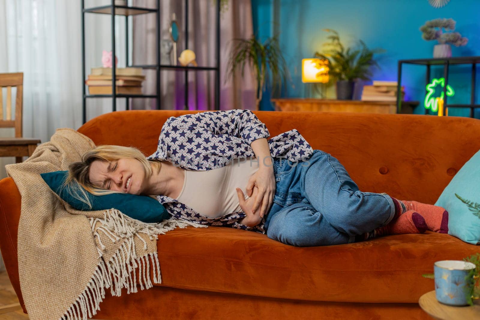 Upset young woman embracing belly suffering from stomachache lying on sofa. Unhappy sad Caucasian girl having menstrual painful feelings, resting on couch. Gastritis, abdominal or period pain concept.