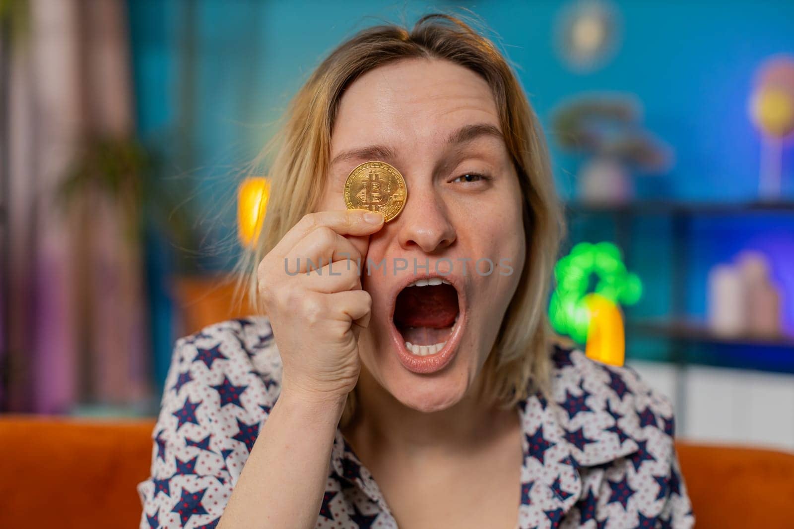 Excited amazed happy woman holds gold BTC coins at home successful developer programmer. Girl stock trader earning bitcoins after online monitoring trading operations. Increasing wealth covering eyes