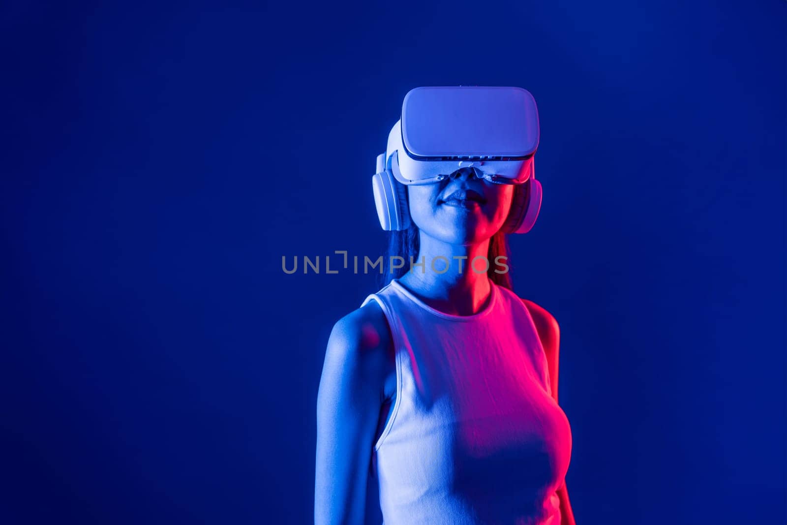 Smart female stand with surrounded by cyberpunk neon light wear VR headset connecting metaverse, futuristic cyberspace community technology. Elegant woman look generated virtual area. Hallucination.