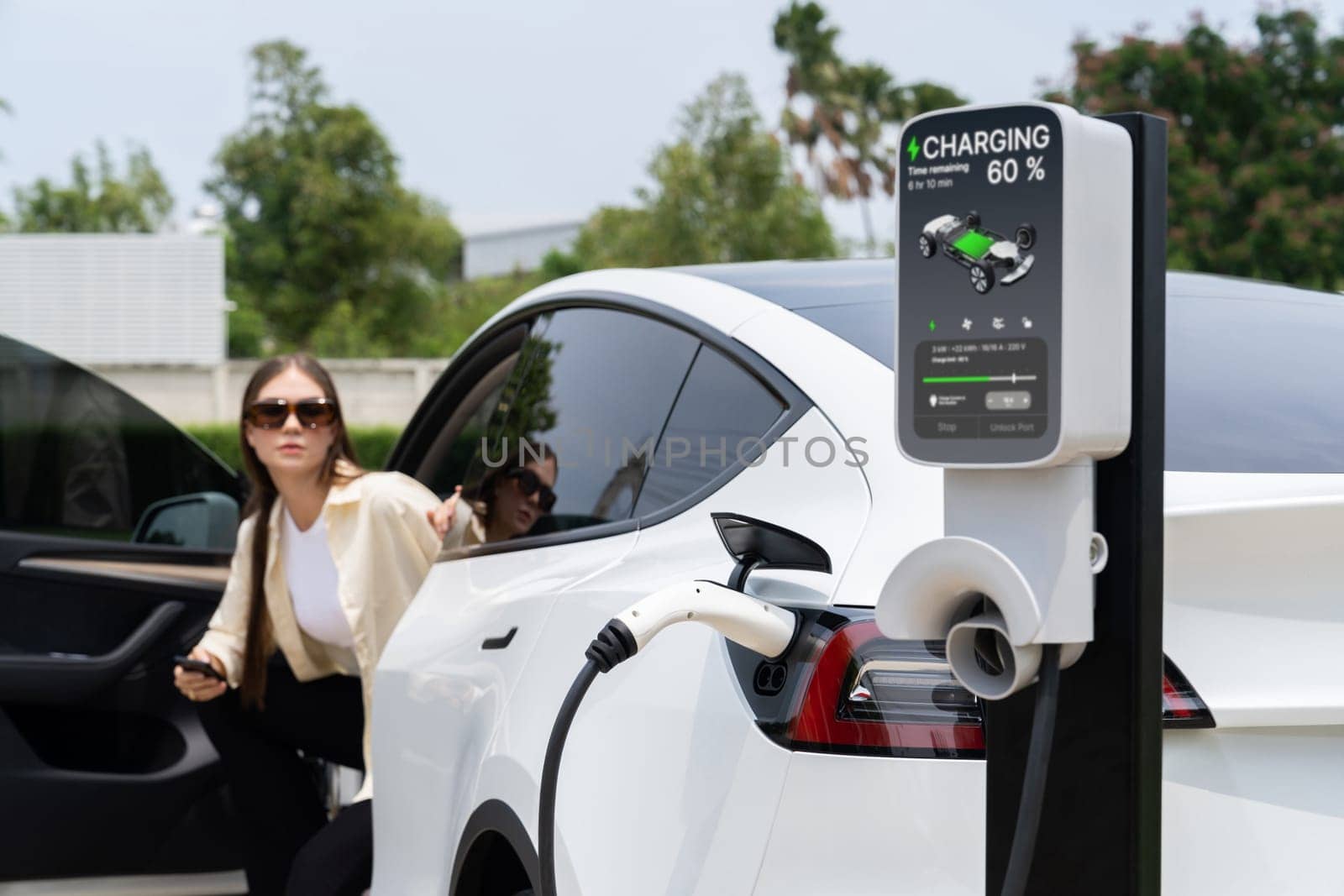 Young woman recharge her EV electric vehicle at green city park. Expedient by biancoblue