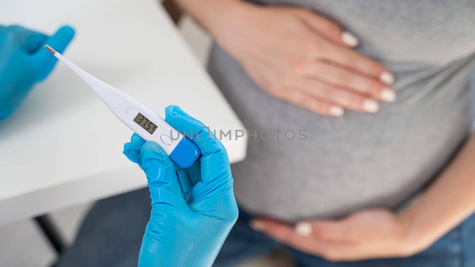 Pregnant woman with fever at doctor's appointment. Therapist holds an electronic thermometer with a temperature of 37.5