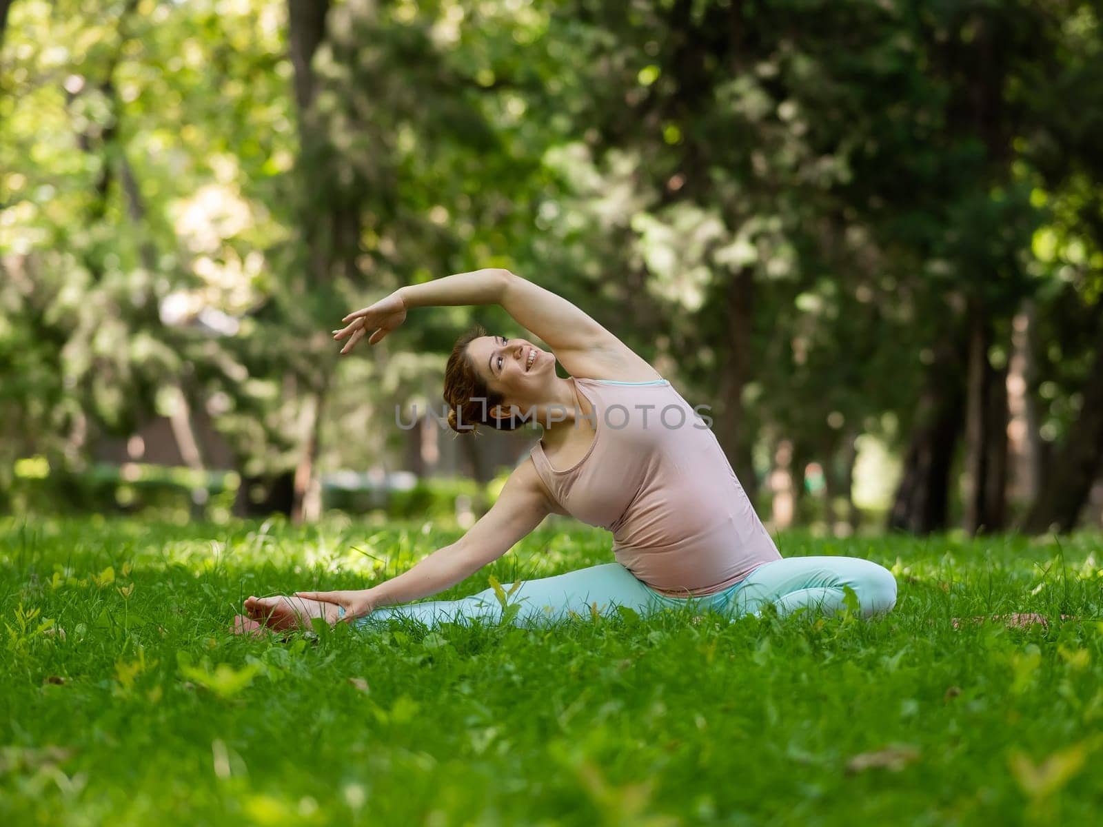 Pregnant caucasian woman doing yoga in the park. Lateral tilt. by mrwed54