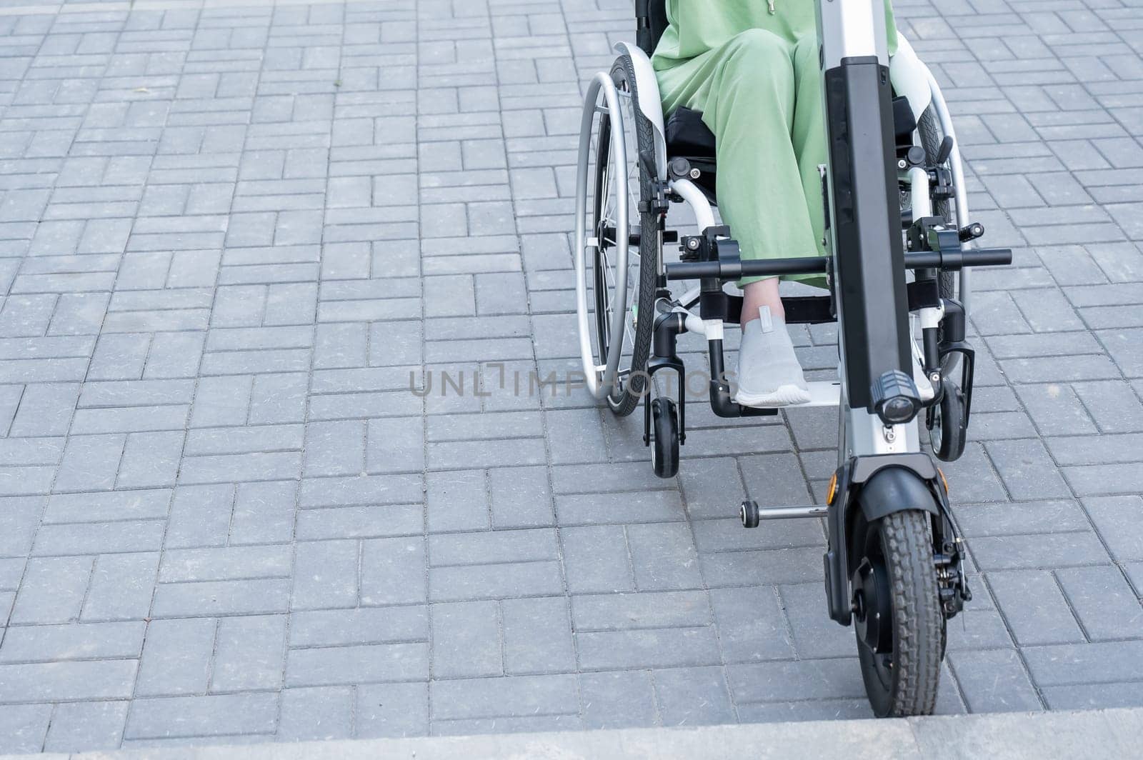 A faceless woman in a wheelchair with an assistive device for manual control. Electric handbike