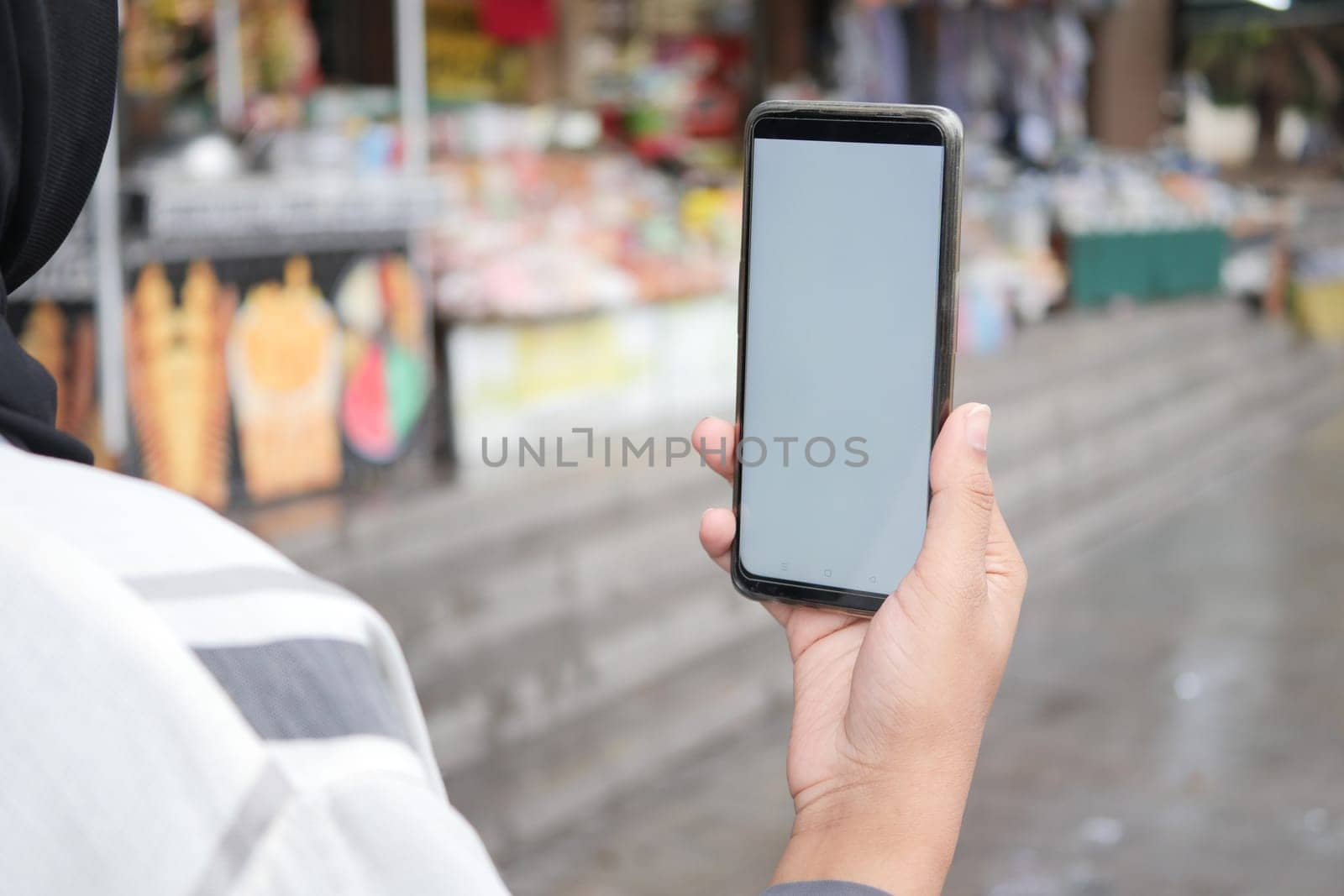 holding smart phone with empty screen with blurred cafe street background.,