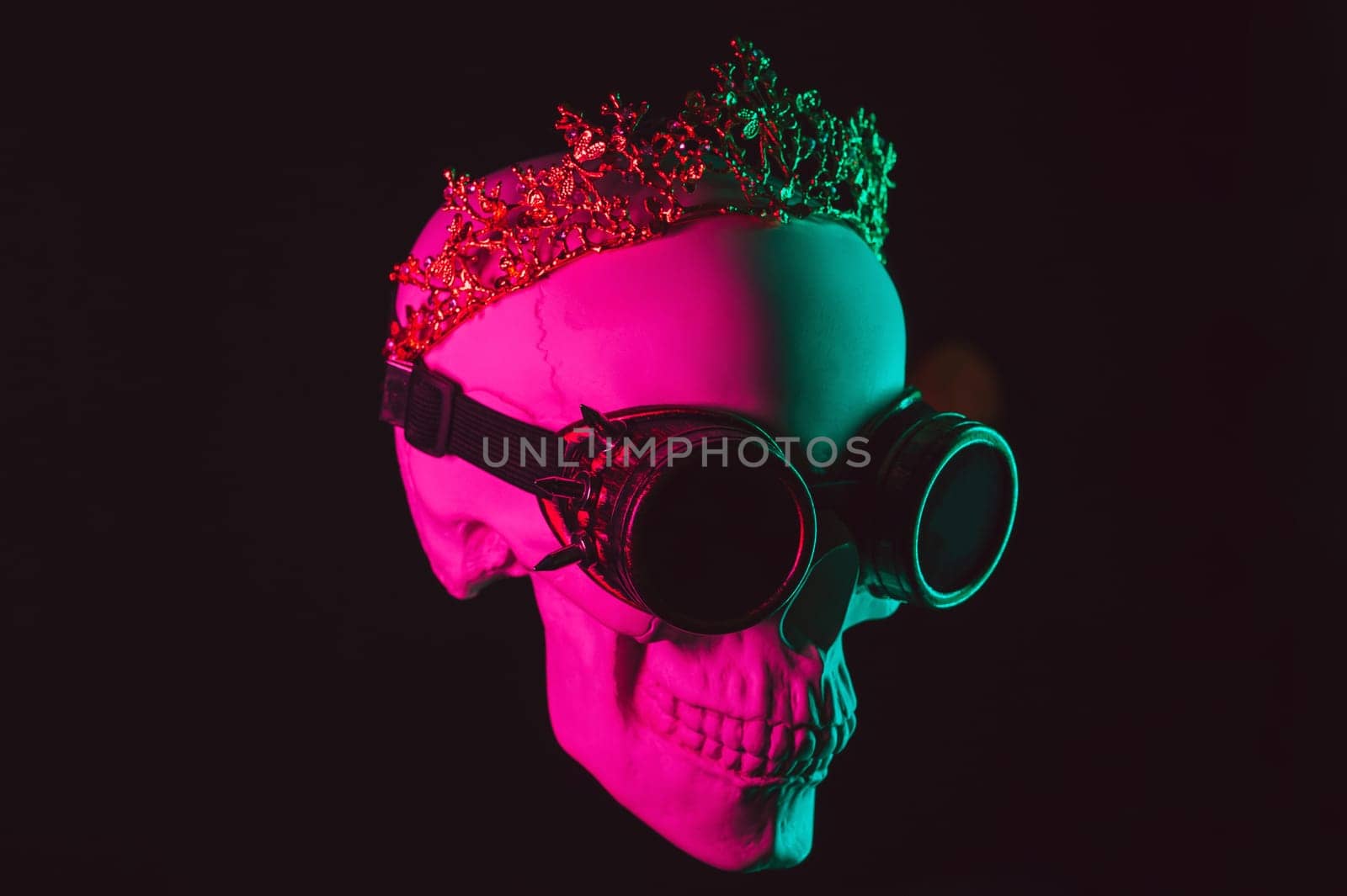 human skull in steampunk glasses and crown with pink green light on black background