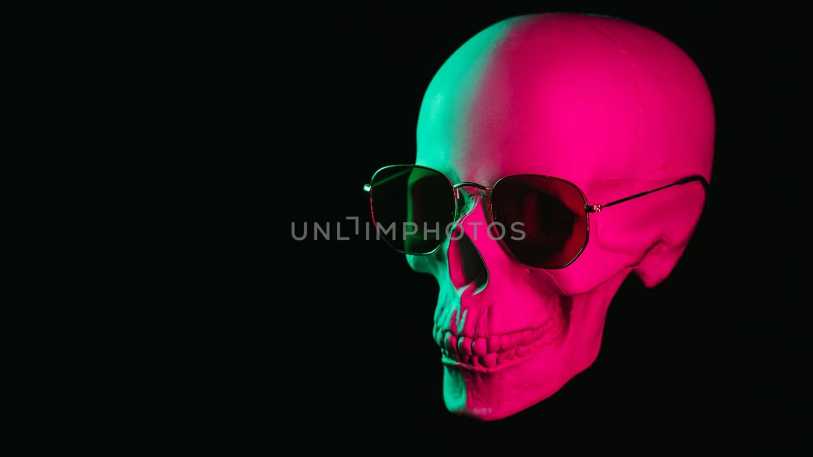 human skull wearing sunglasses with pink green neon light on a black background