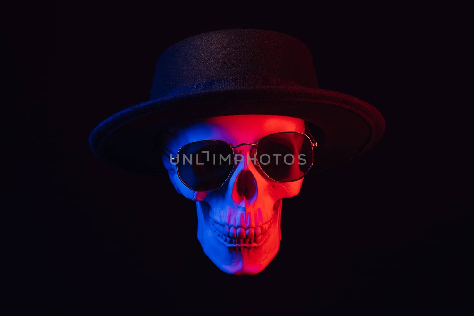 human skull wearing sunglasses and a hat with colored neon light on a dark background