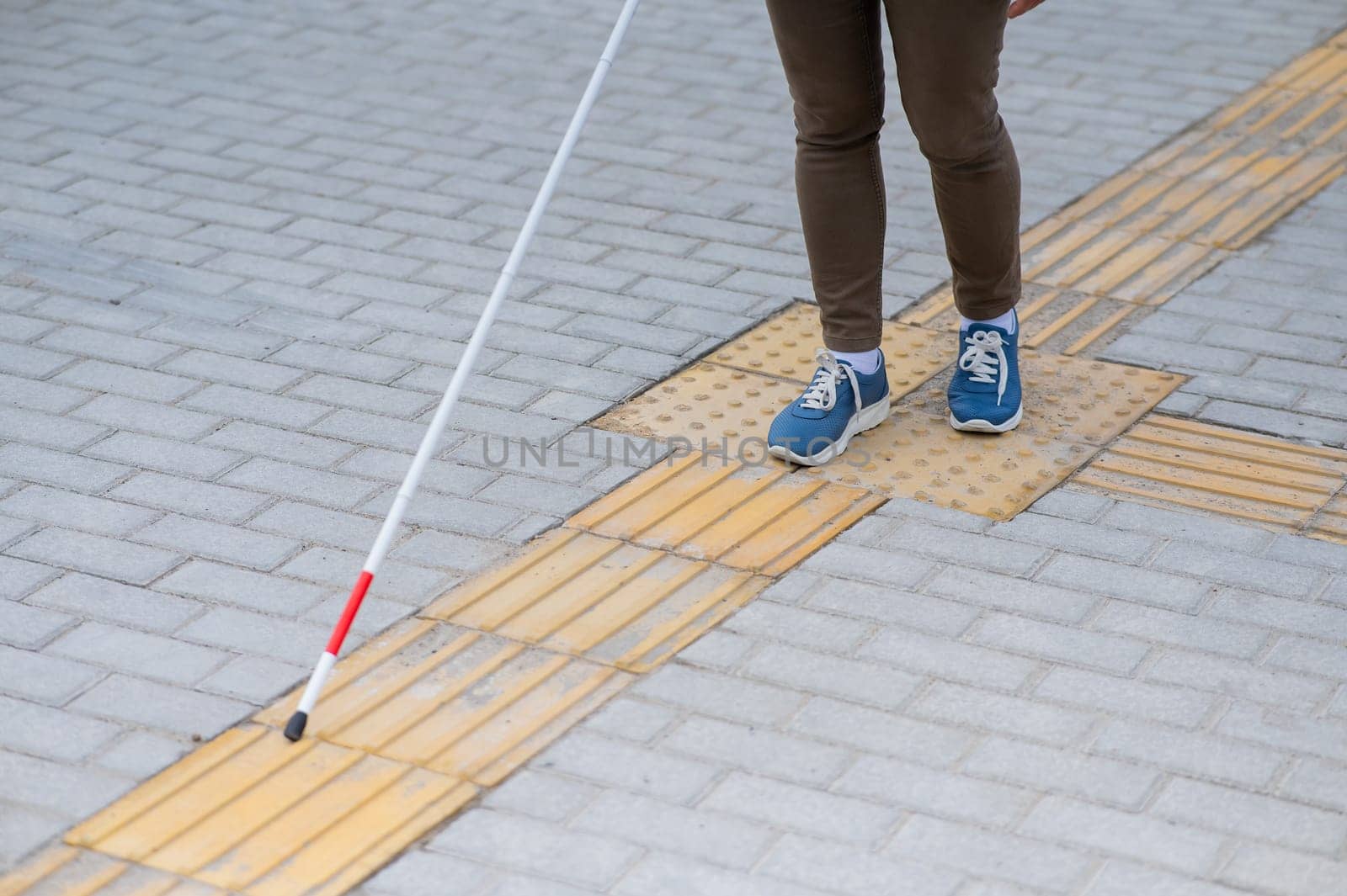 Close-up of a woman's legs with a cane near a tactile tile