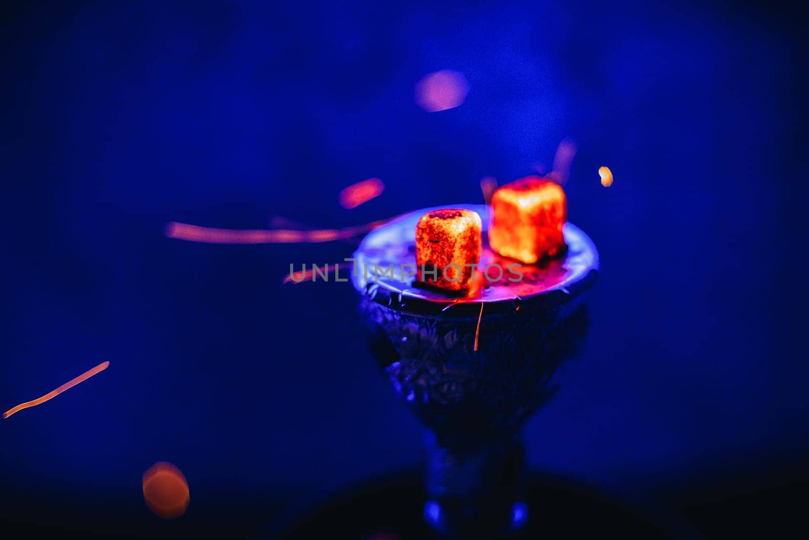 Hot coals on the bowl of the hookah with sparks for a traditional Eastern relaxation and enjoyment on a blue blurred background