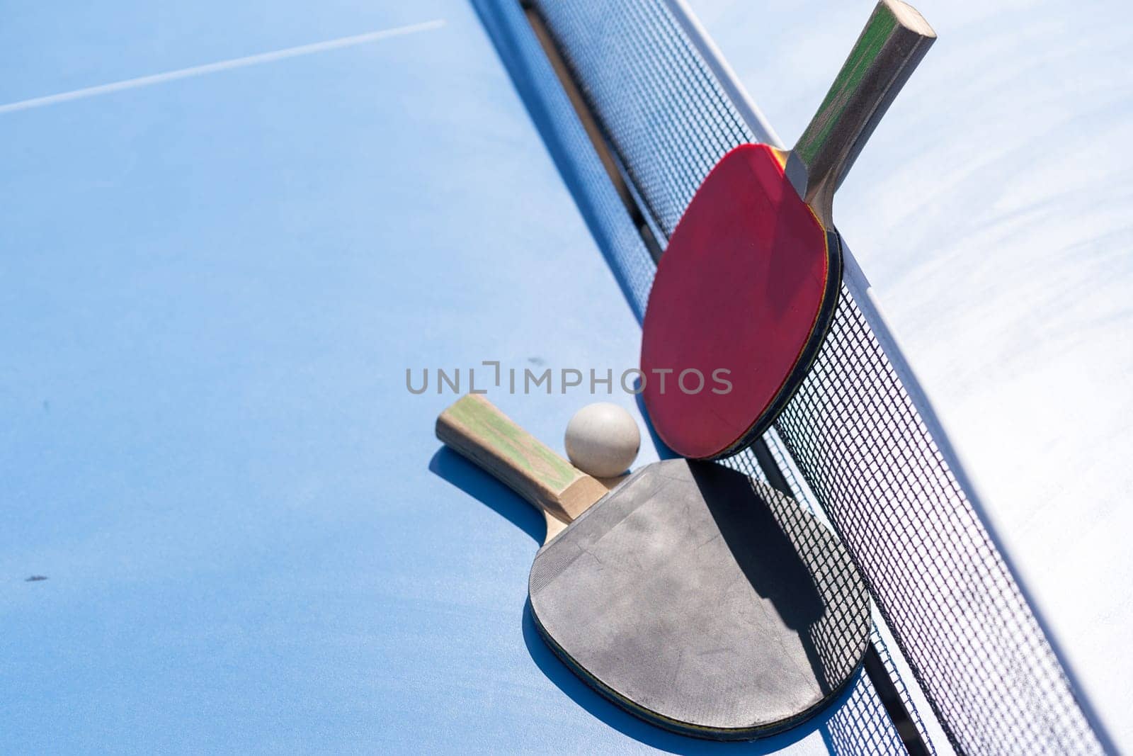 Two table tennis or ping pong rackets and ball on blue table with net. High quality photo