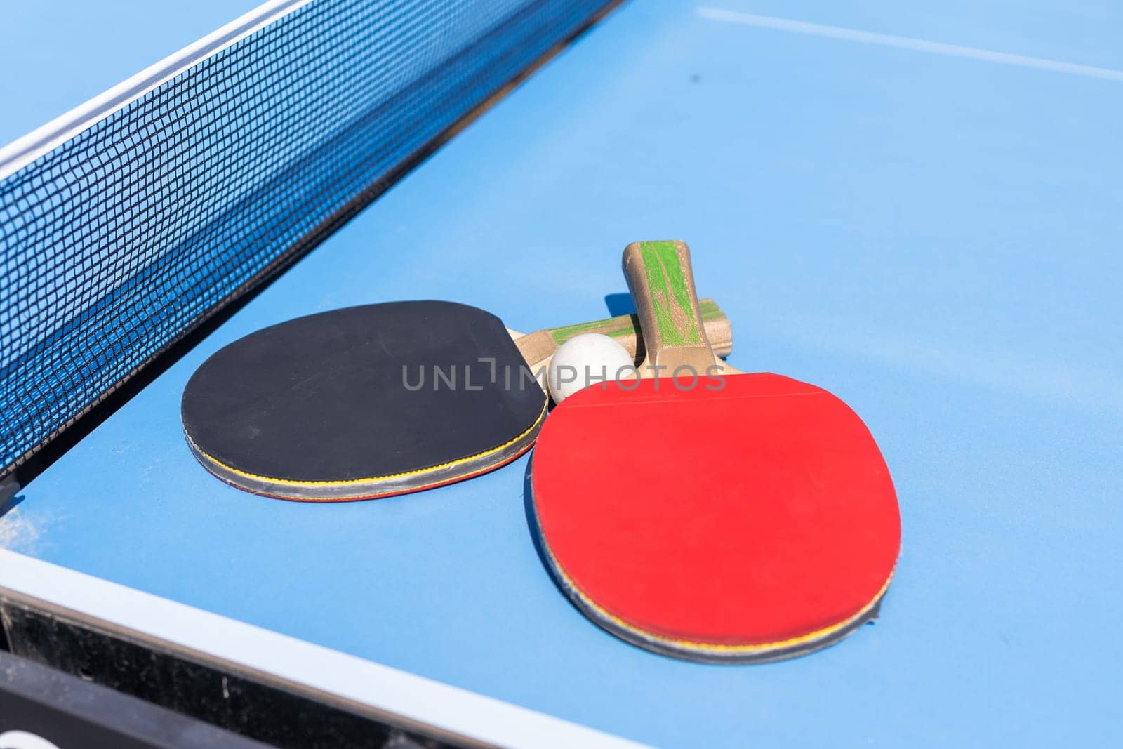 Two table tennis or ping pong rackets and ball on blue table with net. High quality photo