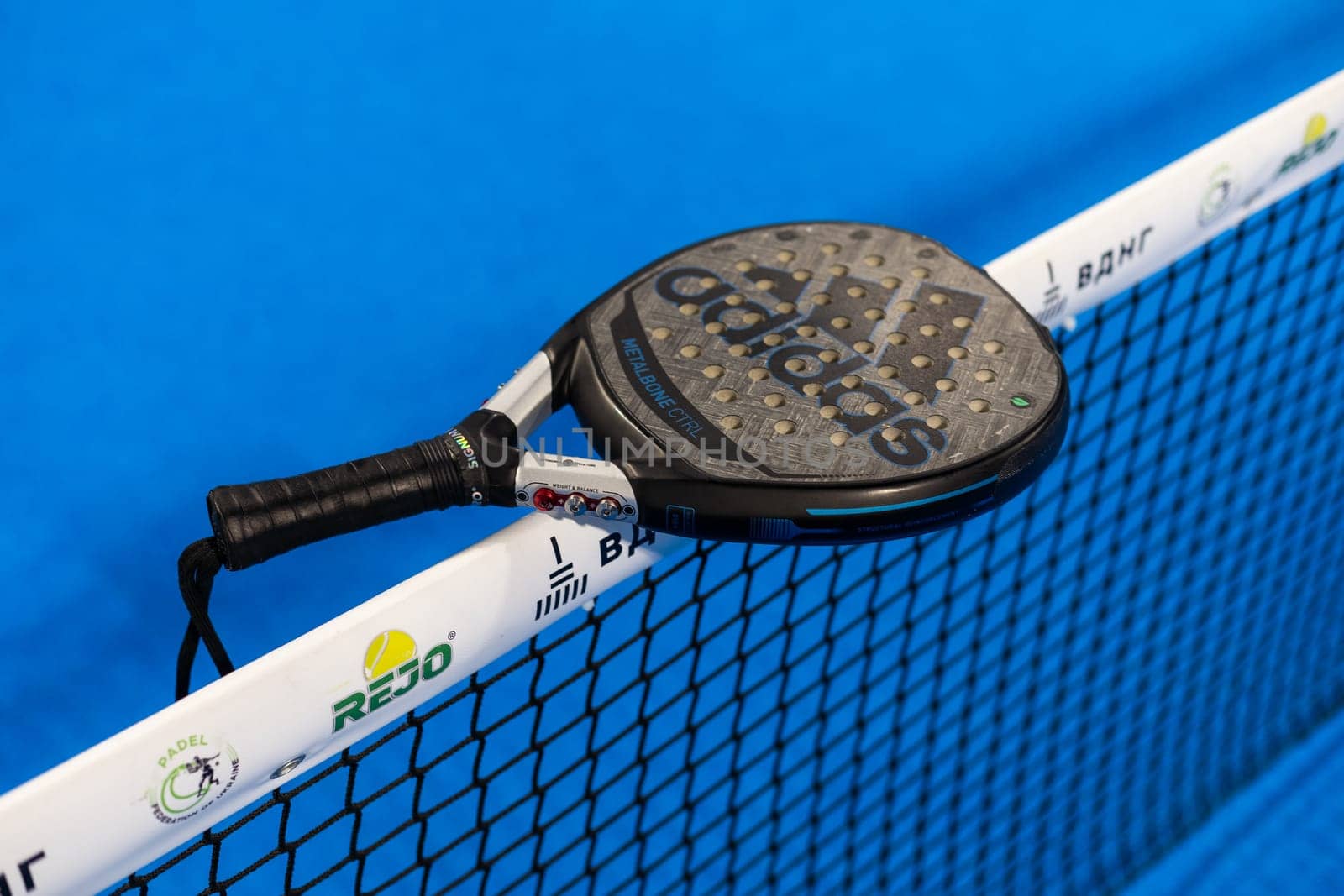 Kyiv, Ukraine, April 18, 2024. Black professional paddle tennis racket and ball with natural lighting on blue background. Horizontal sport theme poster, greeting cards, headers, website and app. High quality photo