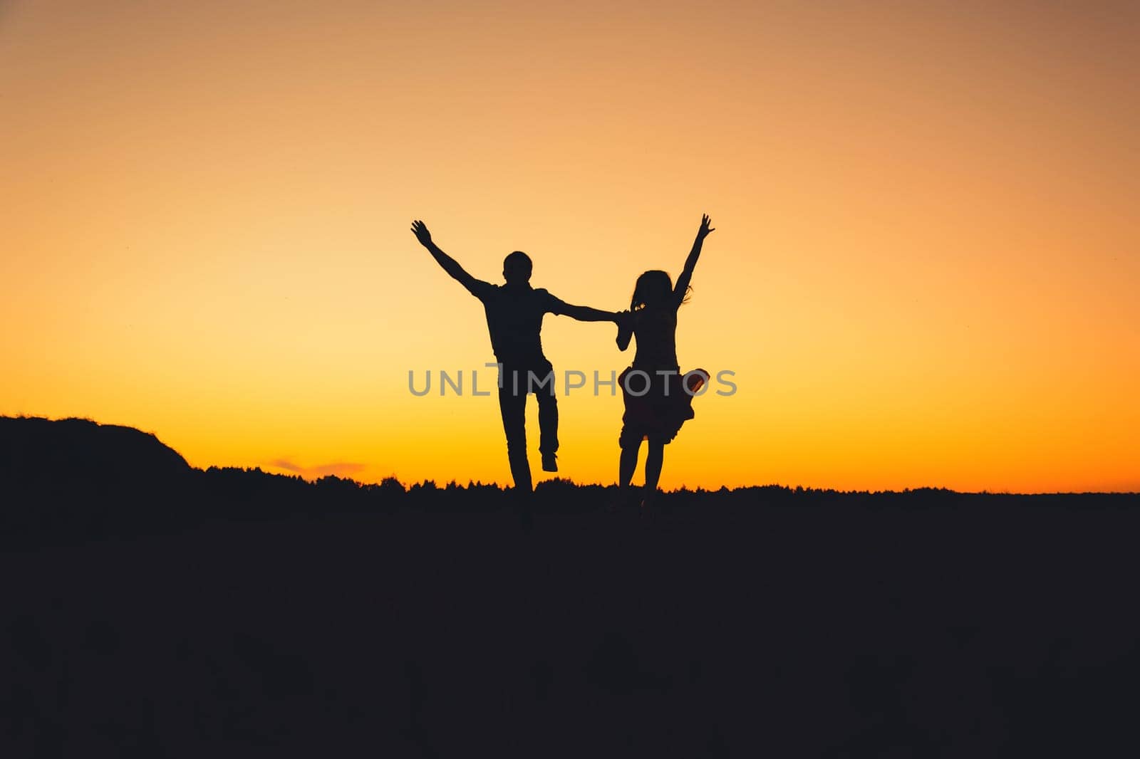 silhouette couples are happily jumping on a background of orange sunset in the summer