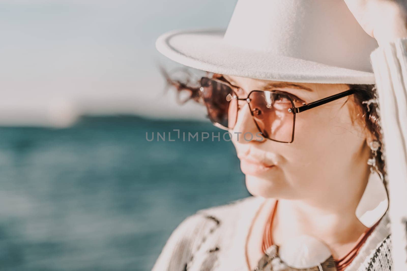 Portrait of a curly haired woman in a white hat and glasses on the background of the sea