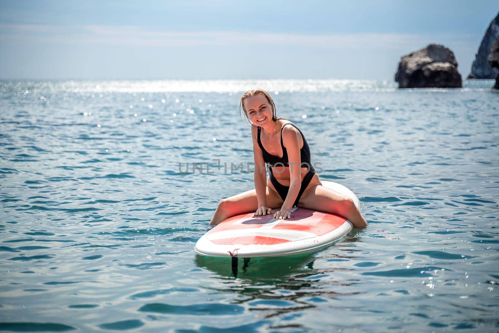 Woman sap sea. Sports girl on a surfboard in the sea on a sunny summer day. In a black bathing suit, he sits on a sapa in the sea. Rest on the sea. by Matiunina
