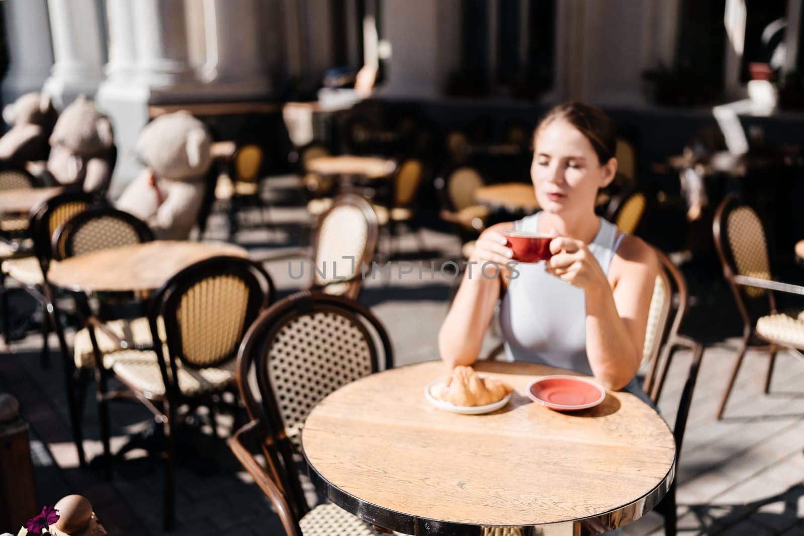 Portrait of happy woman sitting in a cafe outdoor drinking coffee. Woman while relaxing in cafe at table on street, dressed in a white T-shirt and jeans by Matiunina