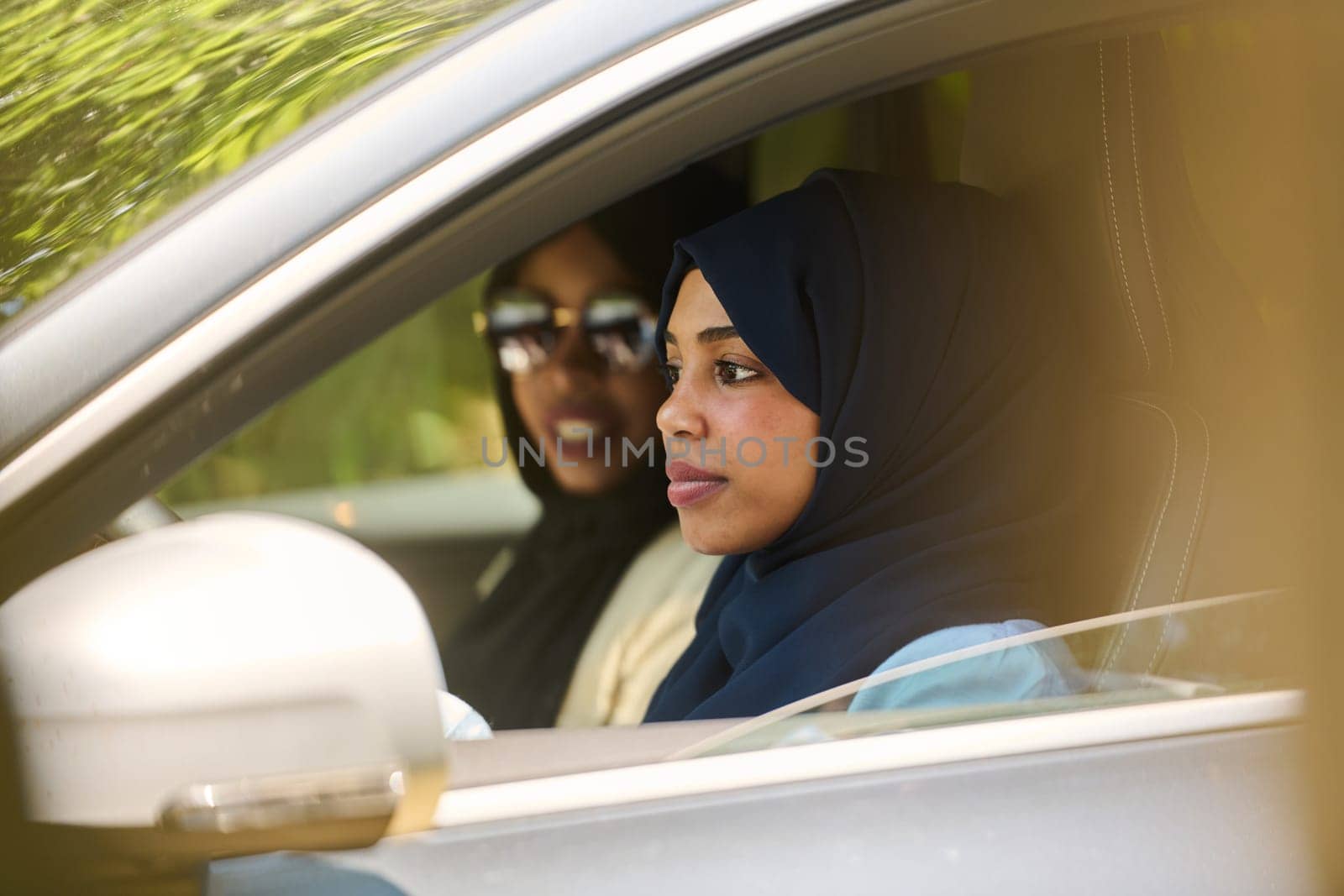 Two Muslim women wearing hijab converse on a smartphone while traveling together in a car through the by dotshock