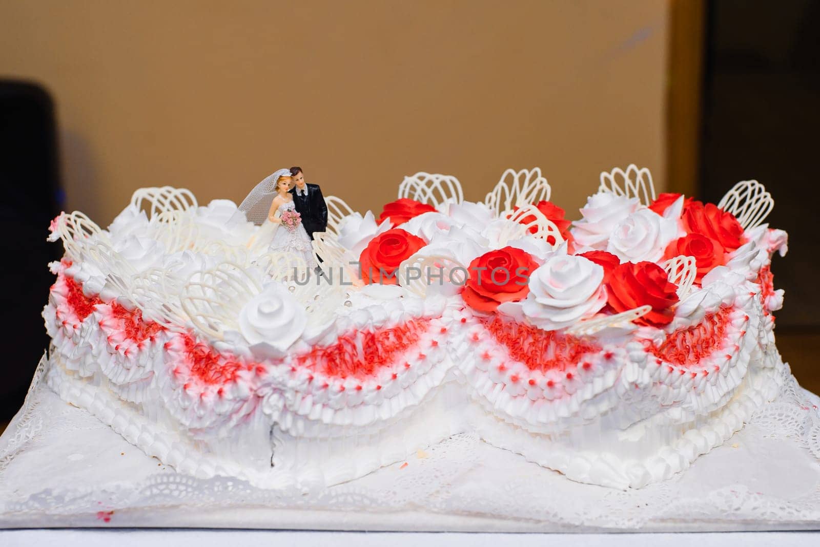 white wedding cake with red flowers cream and puppets of the bride and groom