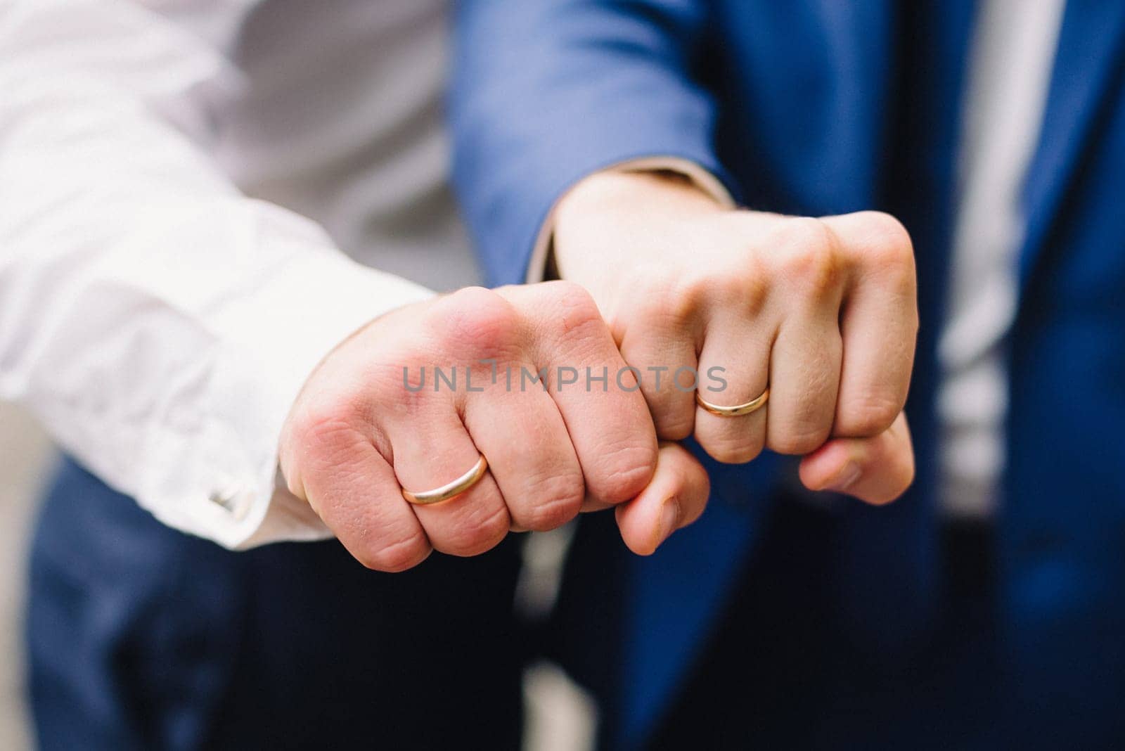hands of two men with wedding gold rings in the shape of a fist
