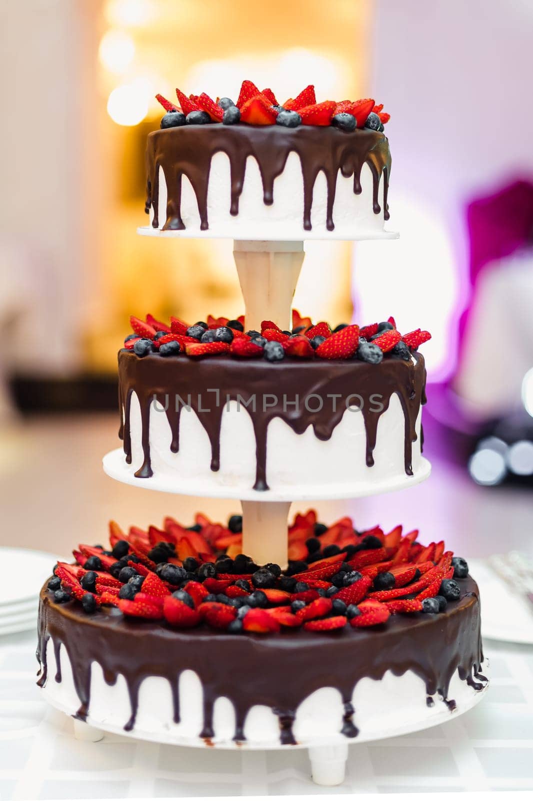 wedding cake in chocolate with strawberries and blueberries on a stand on the table