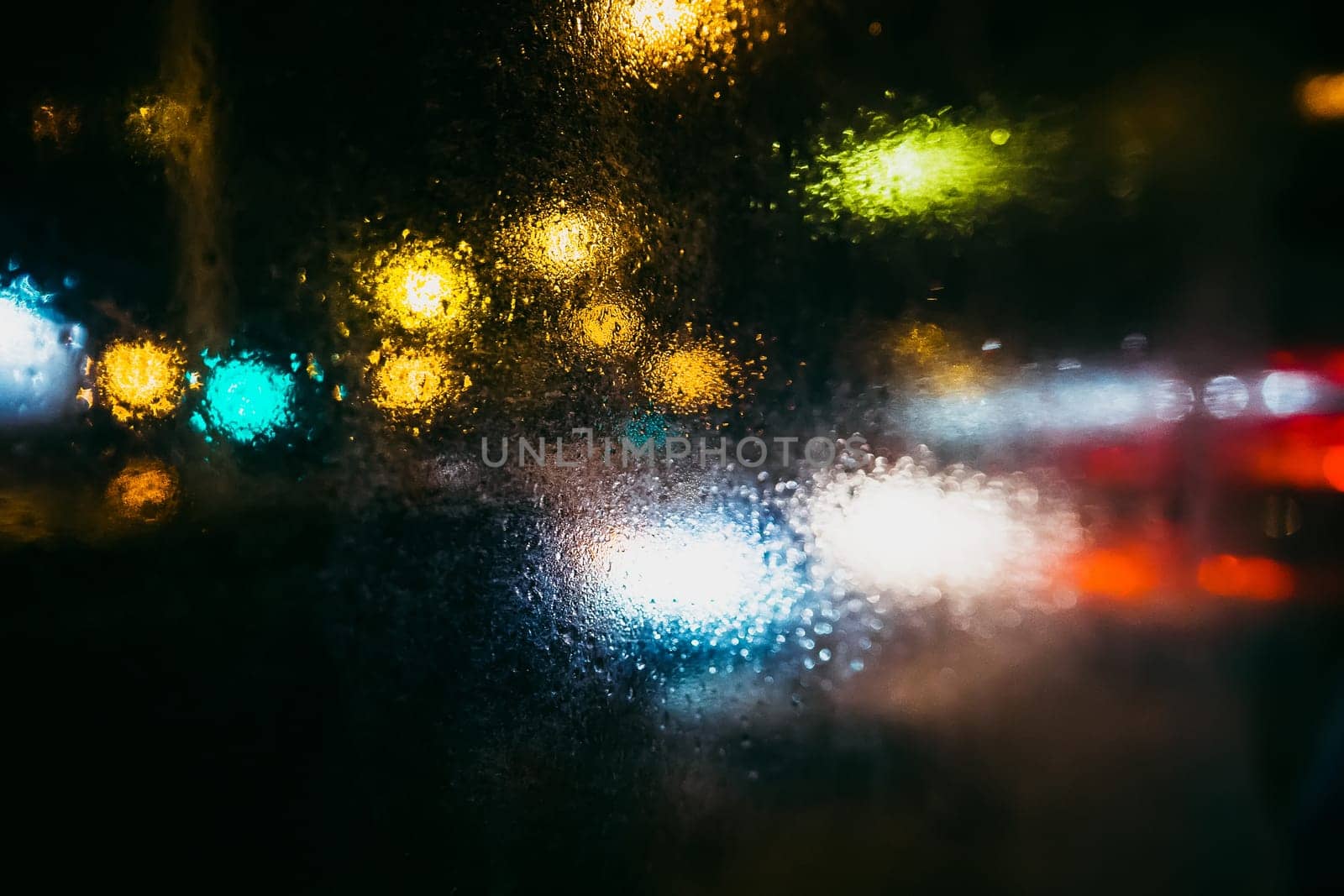 rain drops on glass with blurry background of the city at night with colored lights from the street lamps and cars