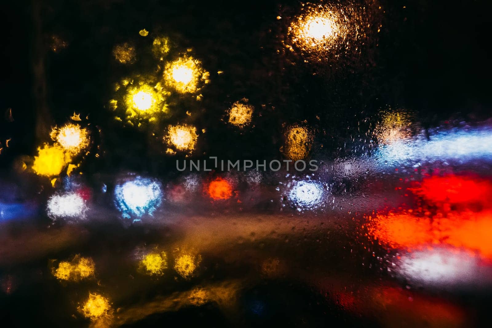 night city with blurred lights from cars and flashlights through the glass with rain drops