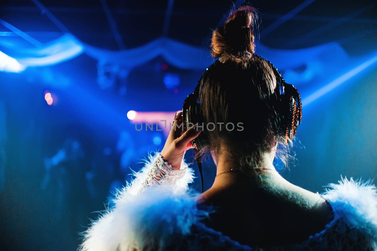 girl DJ headphones play at the concert in the night club music with blue lighting