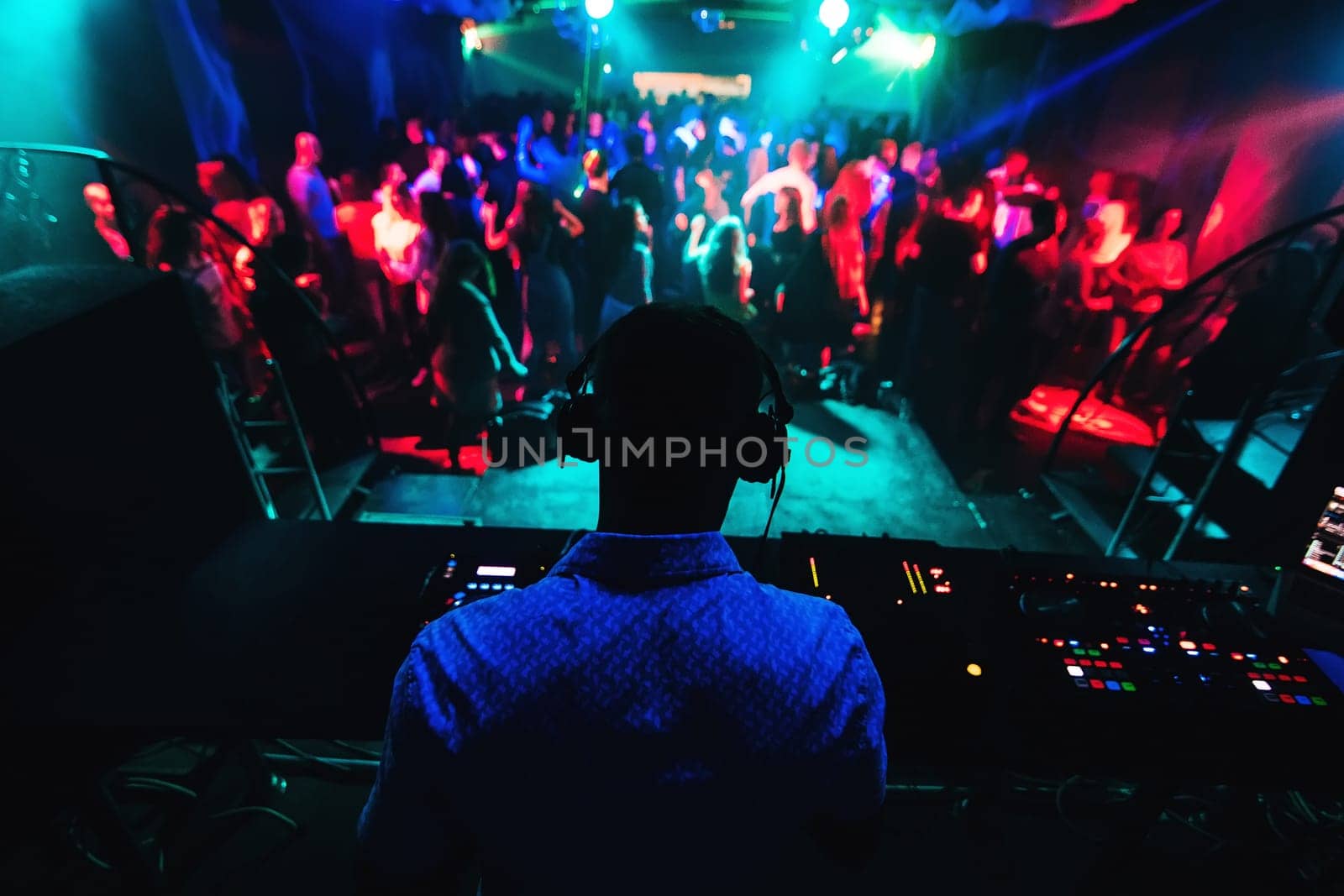 silhouette of a DJ playing music on the mixer and a lot of people dancing in a nightclub on stage with colorful light