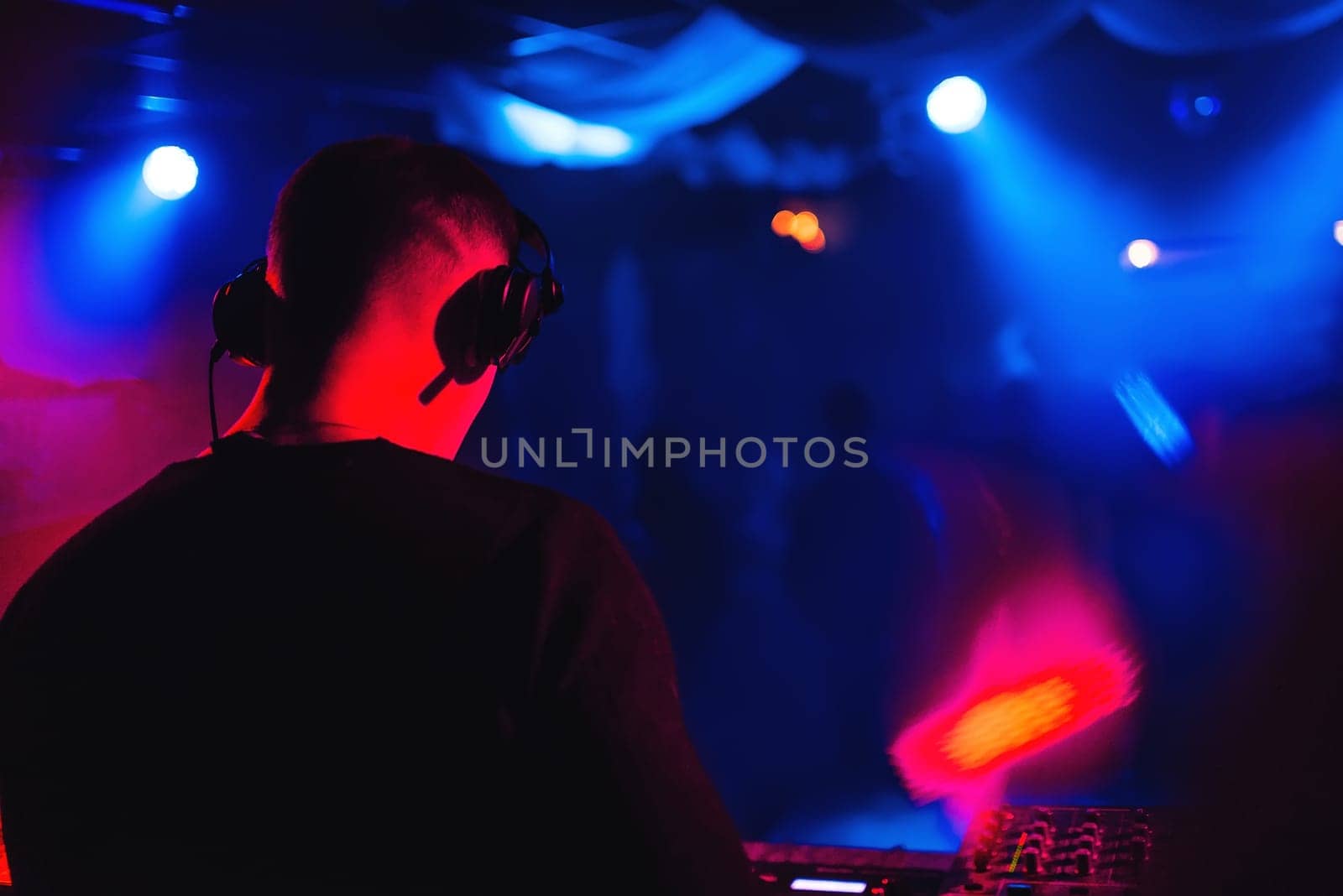 DJ in headphones at the mixer playing the music in a nightclub silhouette with back lighting