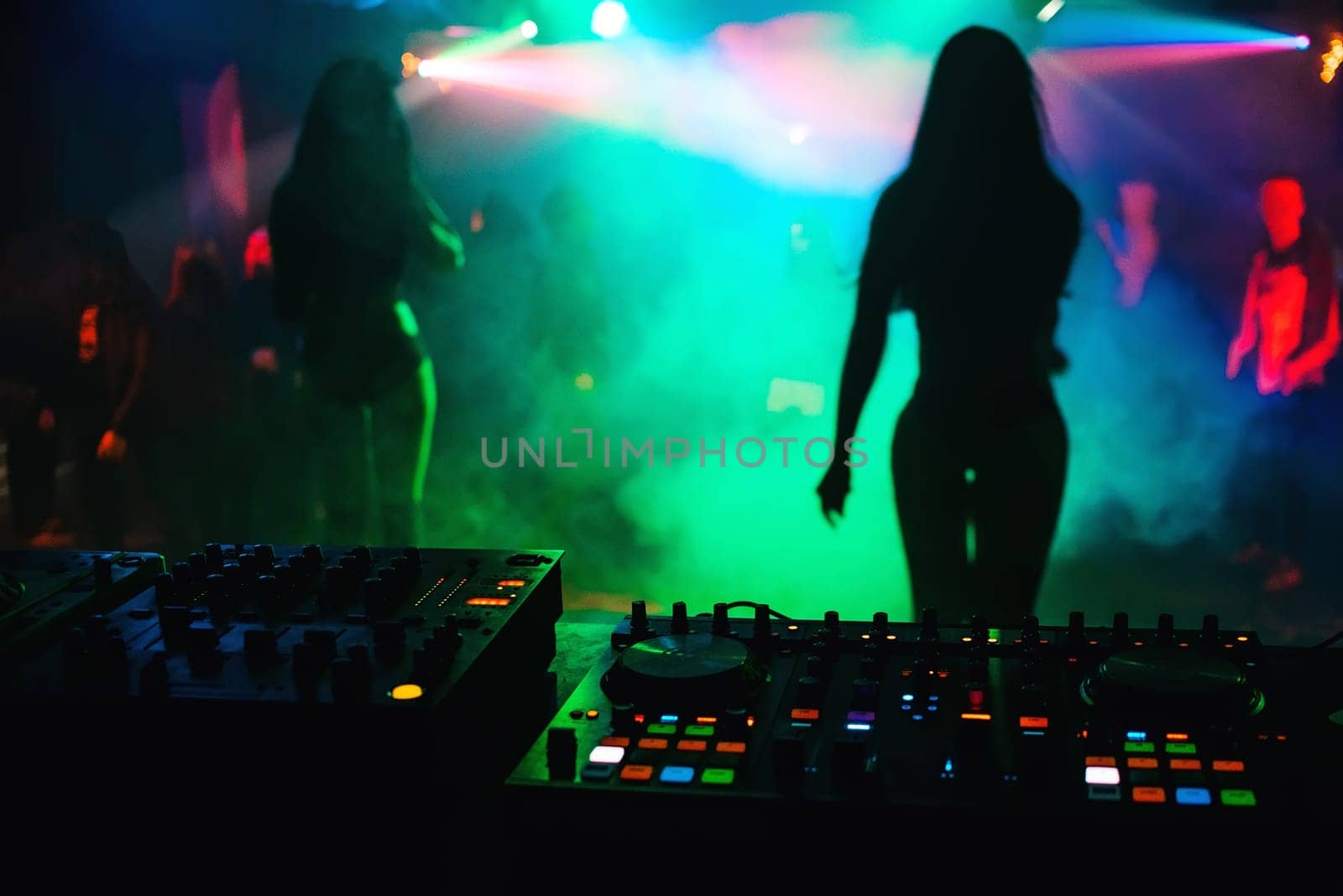 silhouette girls dancers on stage in a nightclub on the background music the mixer DJ with colorful light