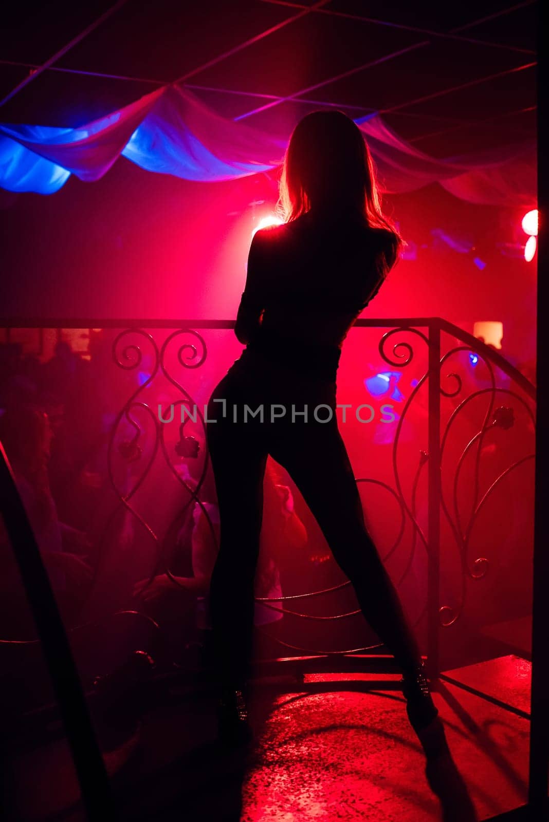 silhouette of young sexy slender girls on the dance floor with a red light night club