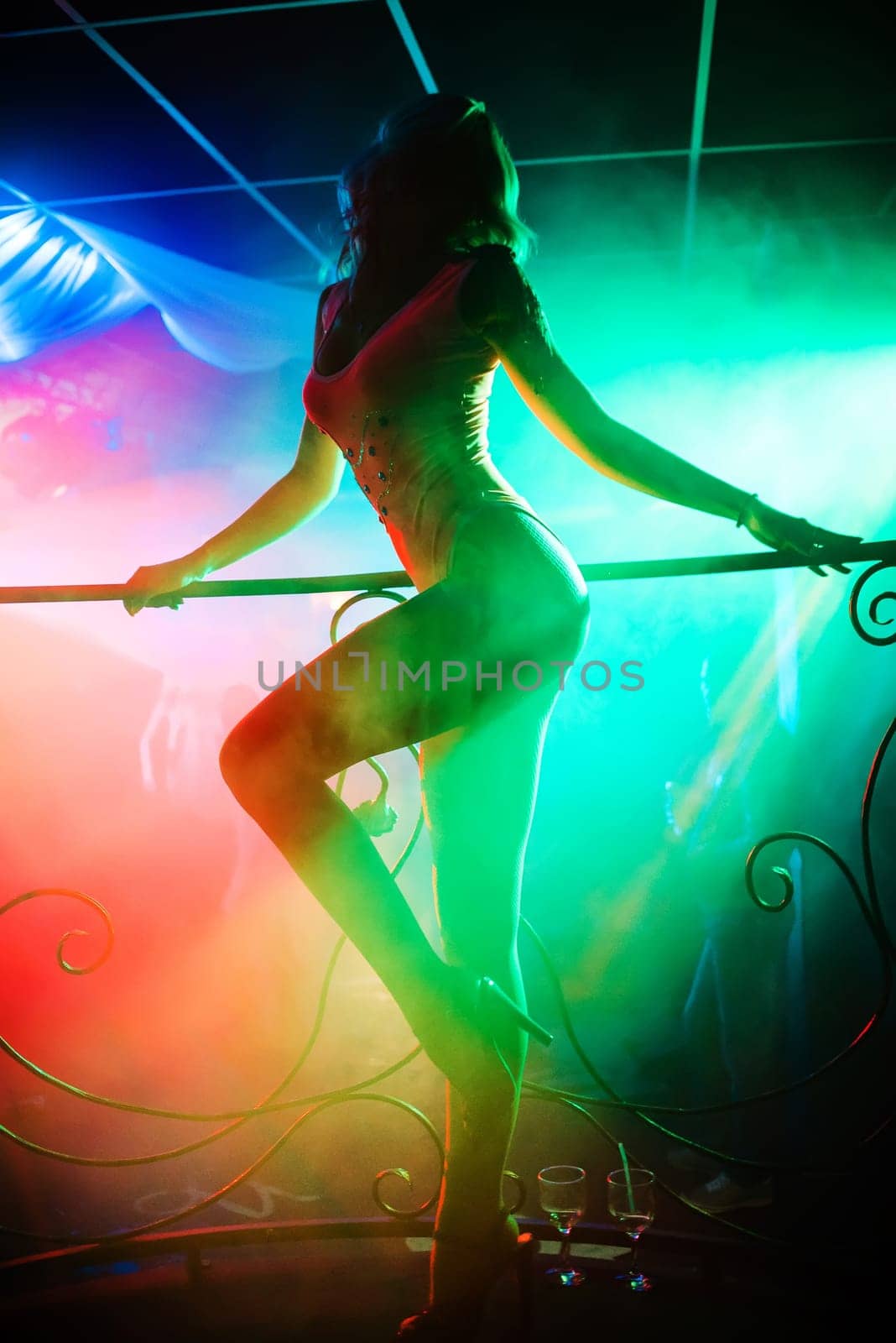 slender young girl dancer with hot body posing nicely on the stage of a nightclub with colored lights