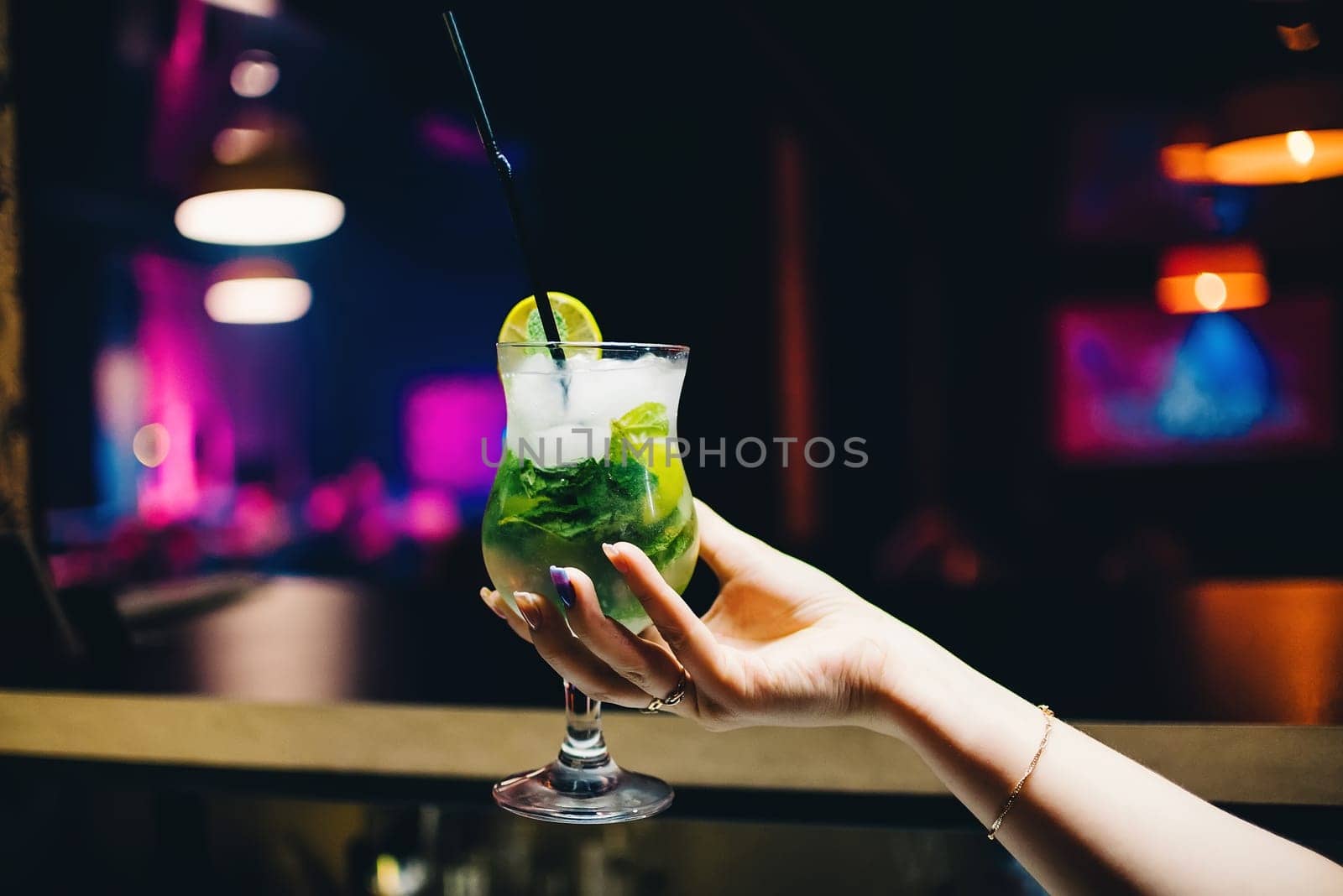 glass of Mojito cocktail in a female hand with a lime and mint with a cooling tube