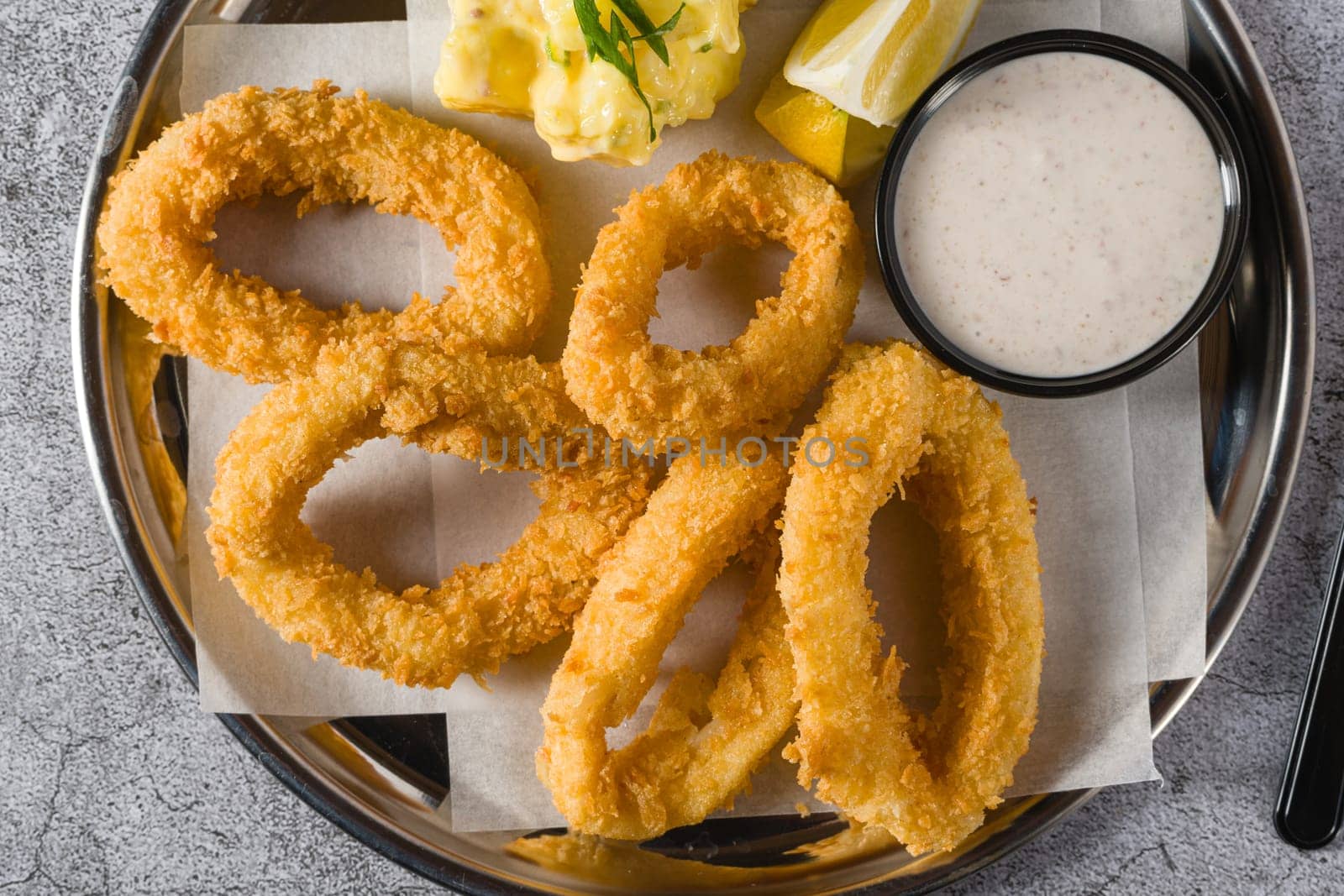 Fried calamari with potato salad next to it on stone table