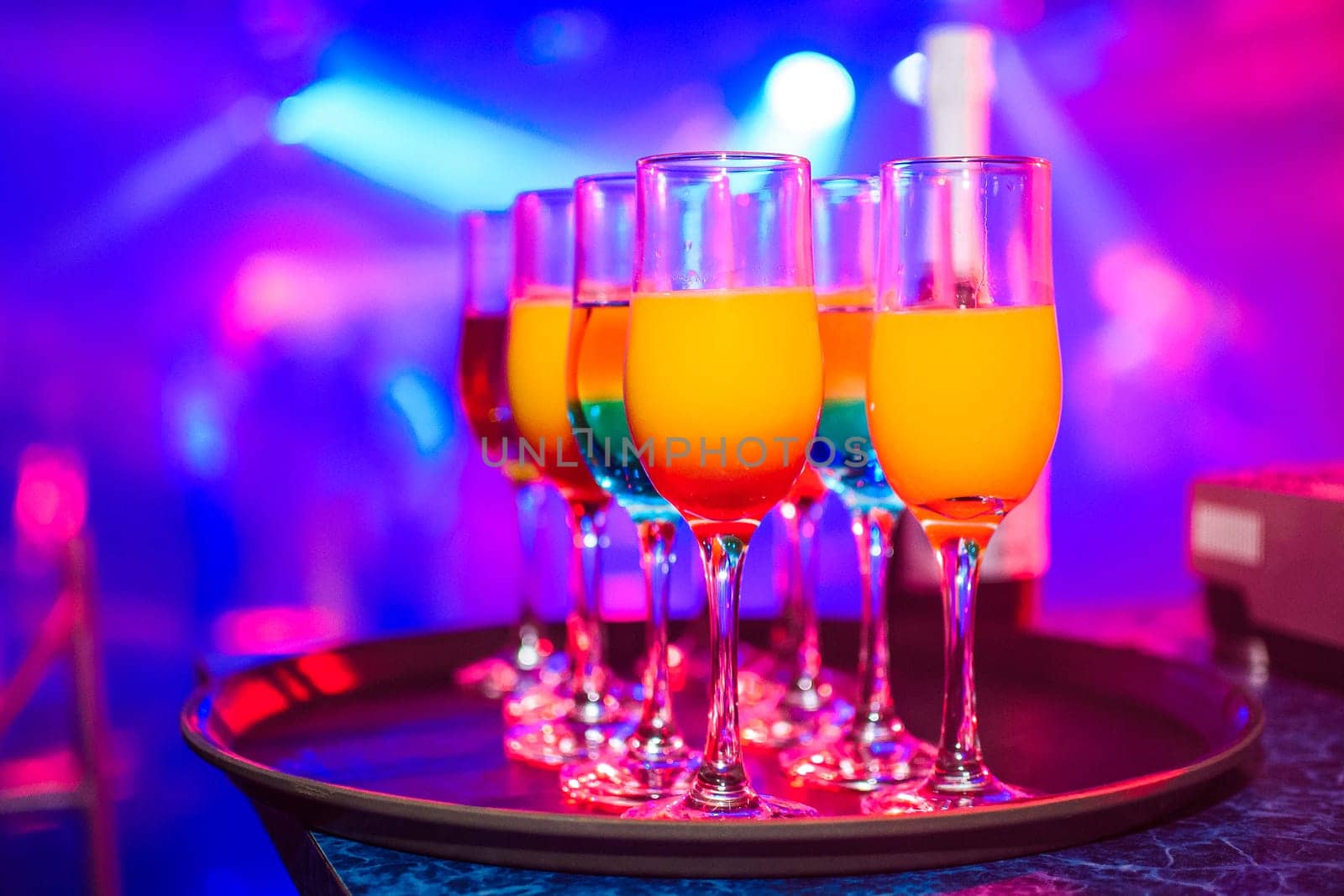 glasses with various alcoholic drinks and cocktails with colored blurred background on the celebration party in the night club