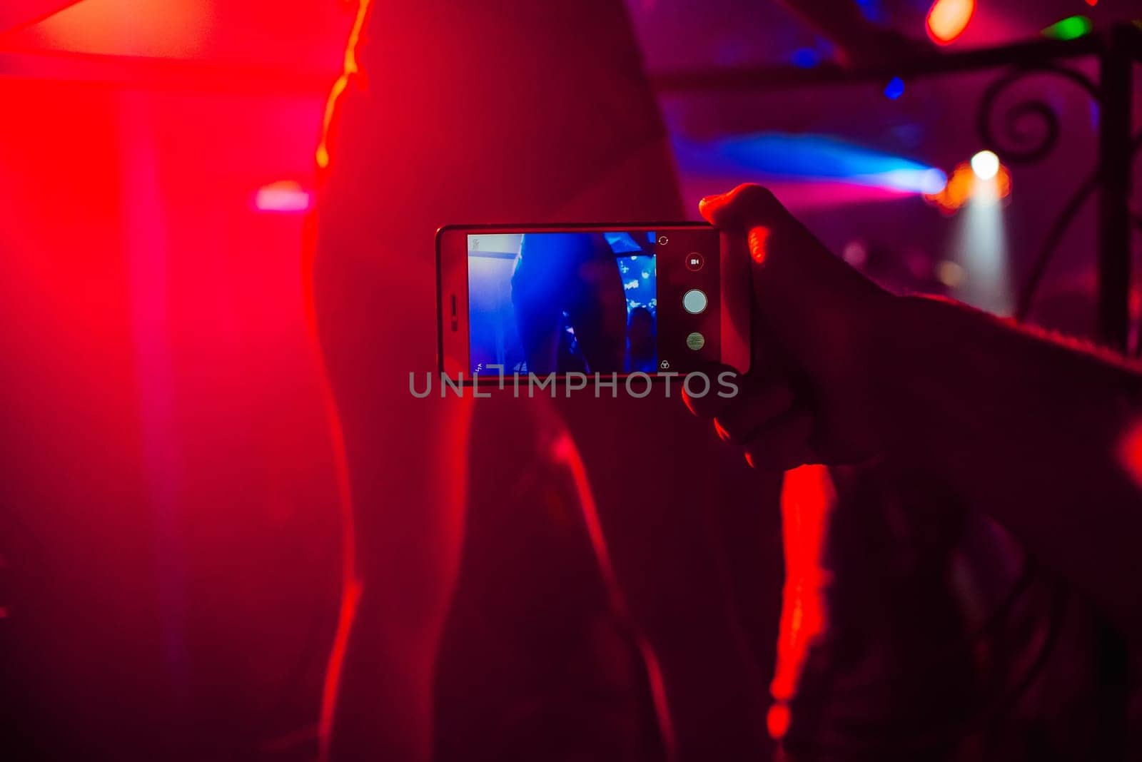 man's hand with a smartphone takes pictures of a dancer's ass in a nightclub