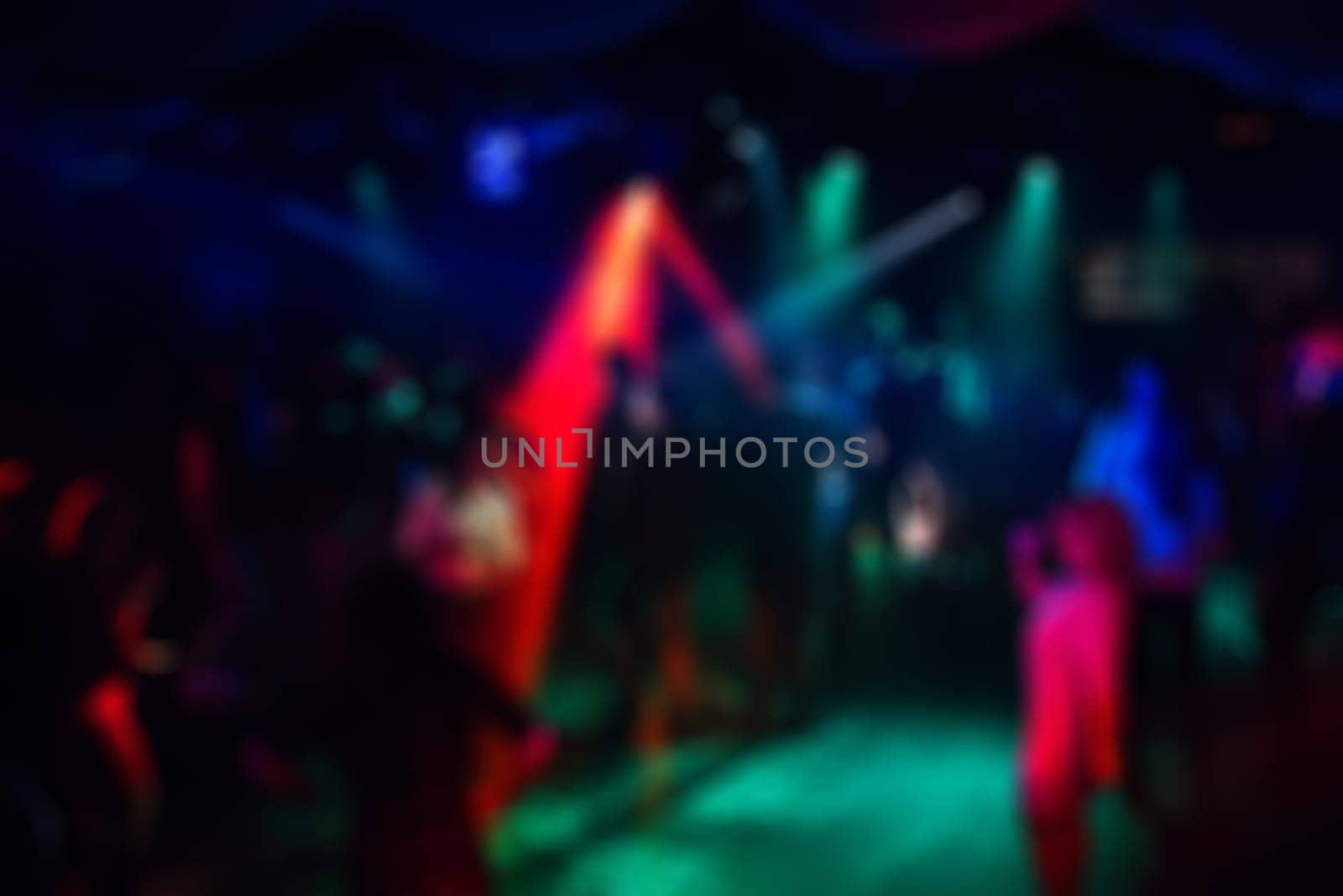 blurred people partying in the nightclub on the dance floor with laser lights