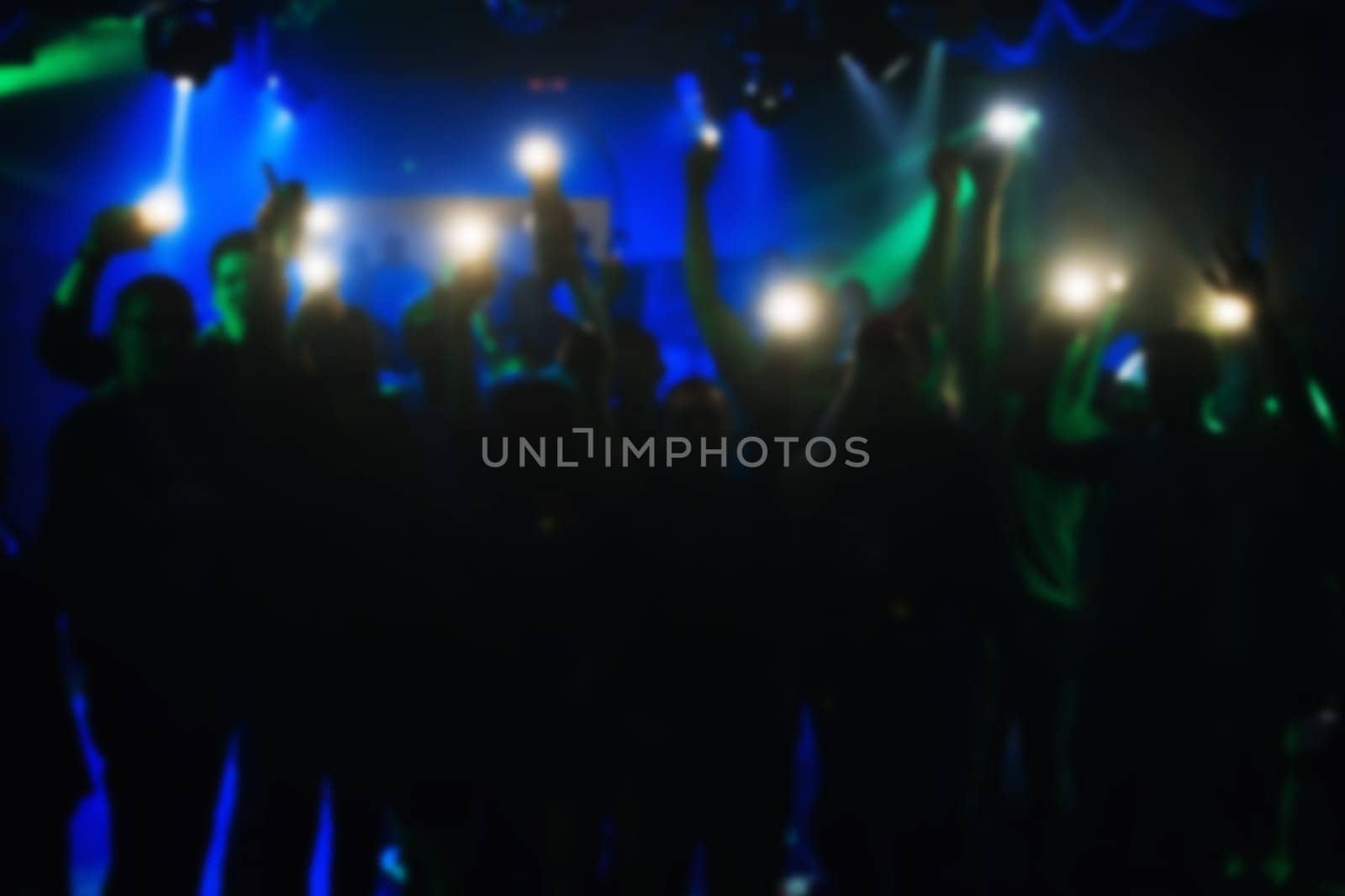 blurred silhouettes of people with lanterns in their hands at the concert in a nightclub