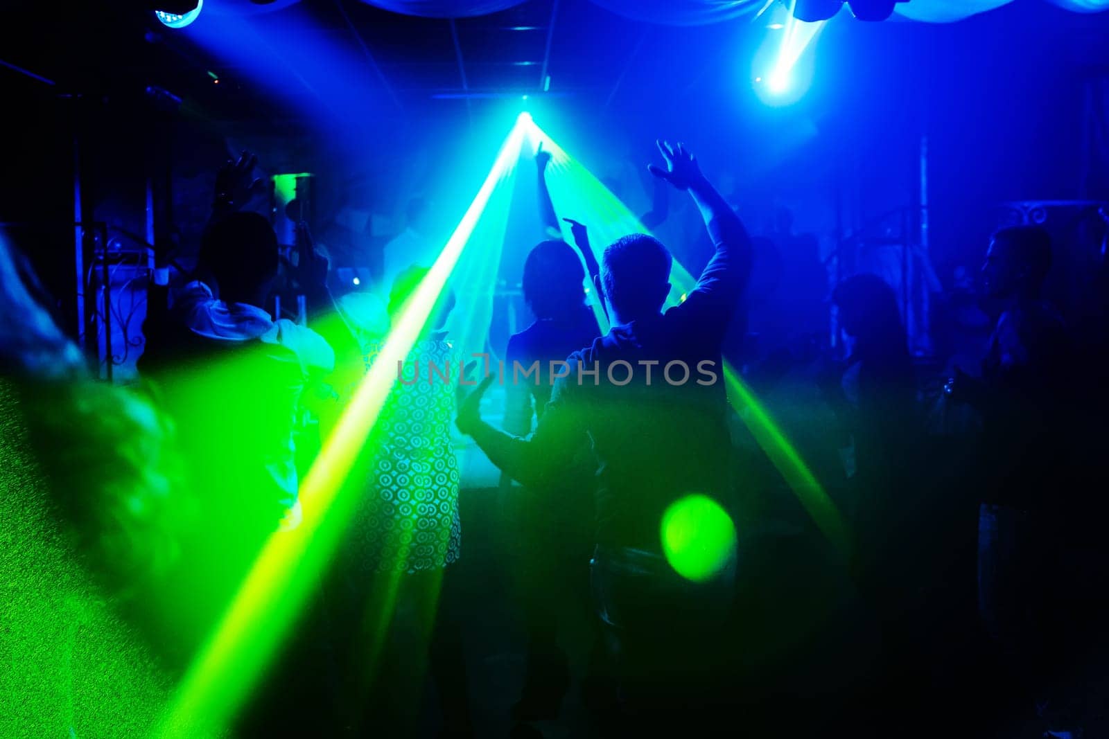 blurred silhouettes of people with their hands up with the laser light in a nightclub