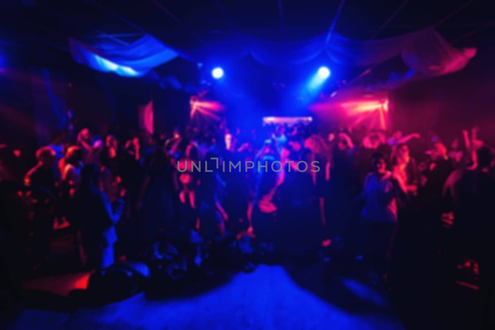 blurred silhouettes of people in the concert hall in a night club under the colourful lighting spotlights