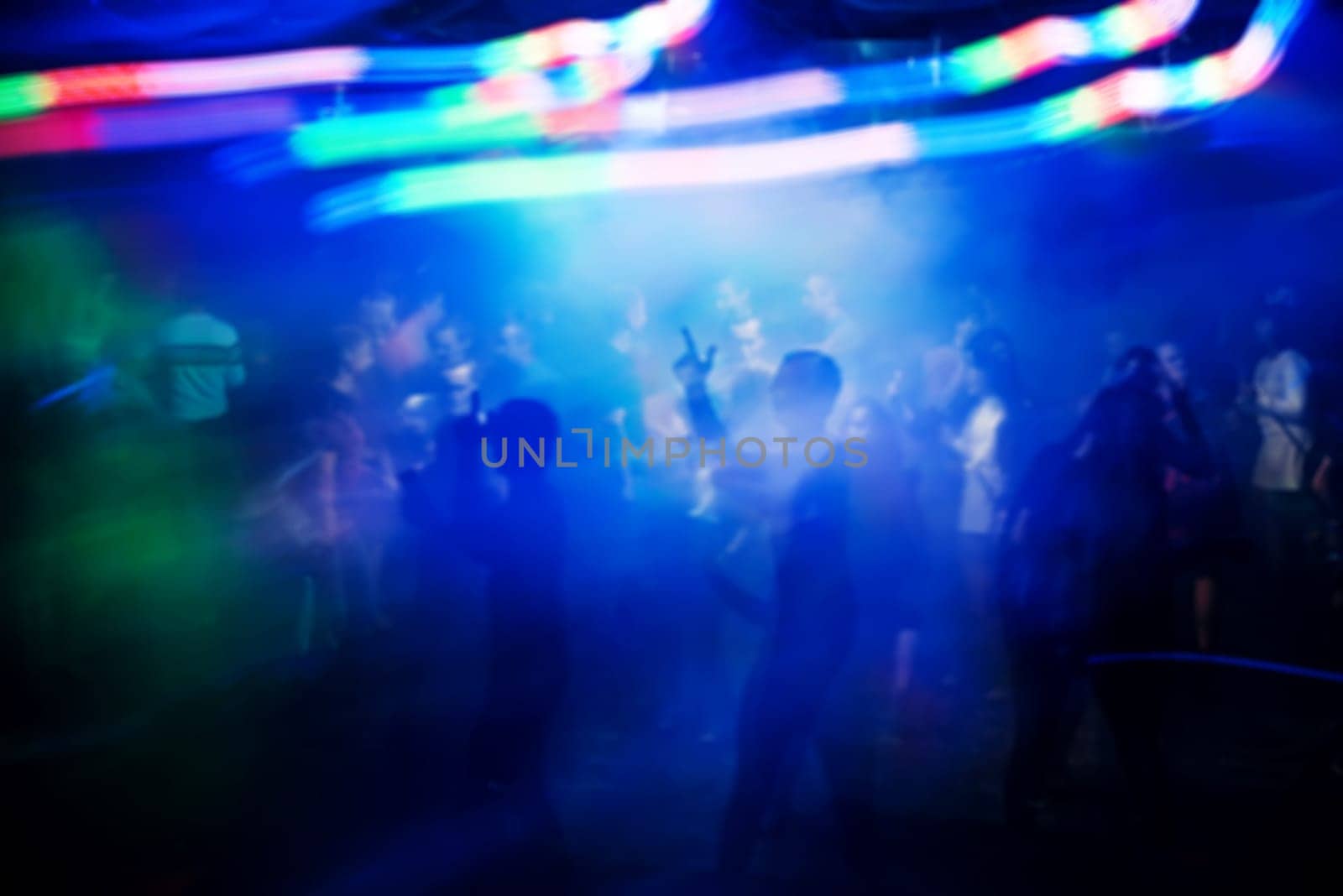 blurred silhouettes of people at the concert at the event with bright multi-coloured light effects