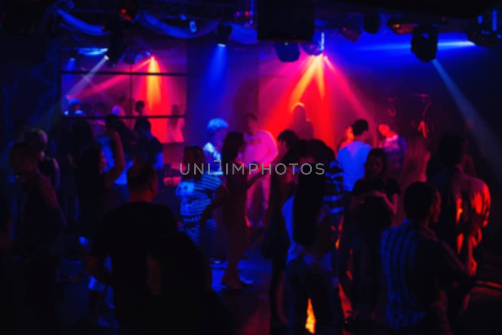 blurred silhouettes of dancing people in night club under the colourful floodlights and spotlights