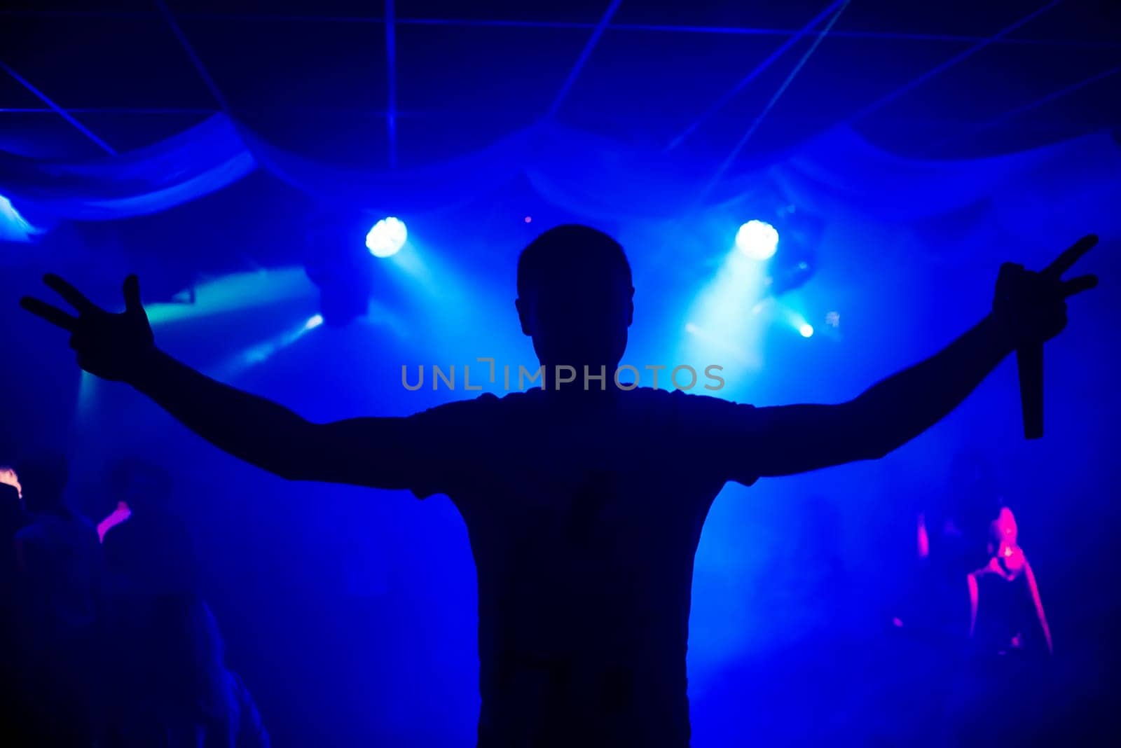 silhouette of a man leading with a microphone on a concert night club with blue smoke and the lights
